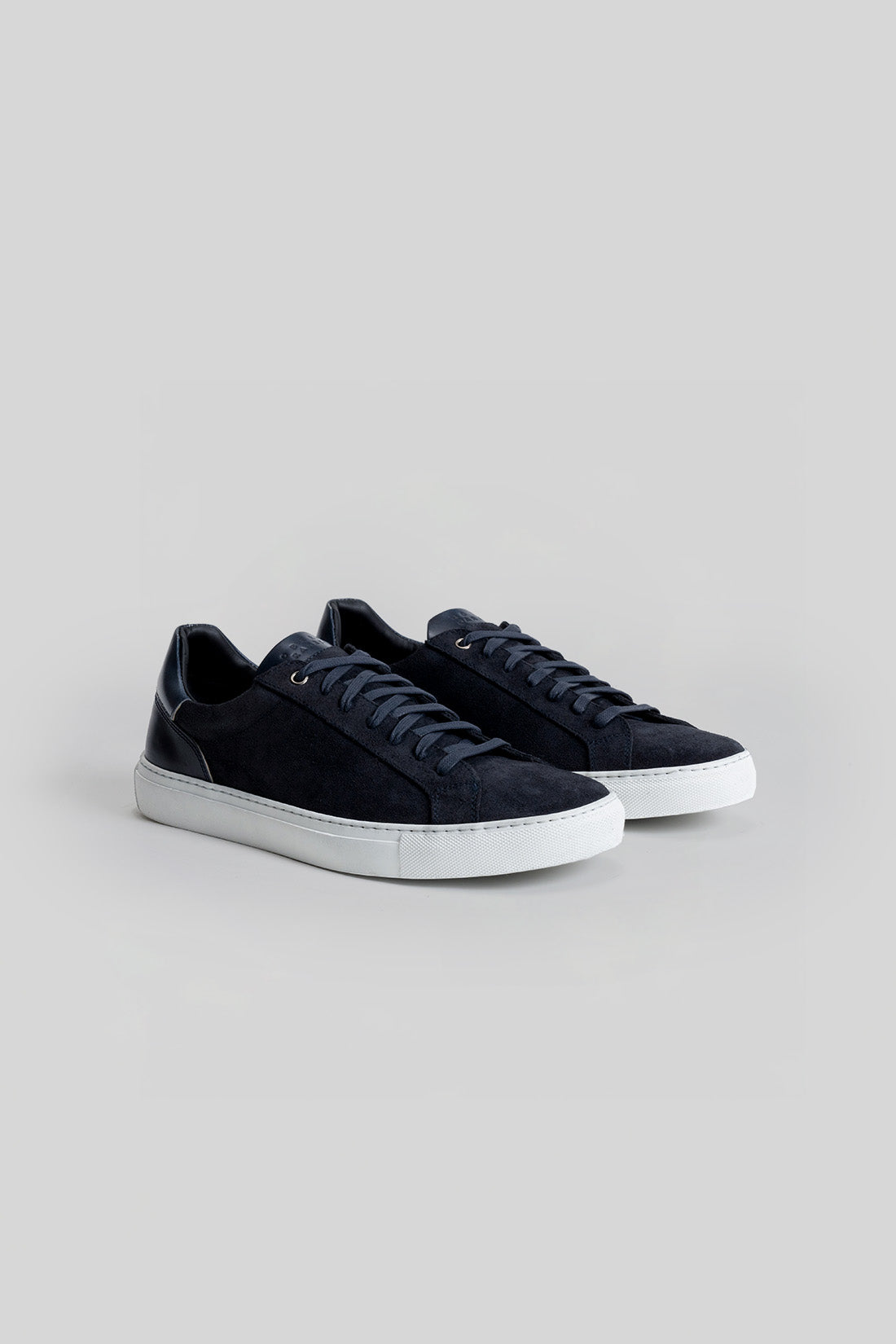 Navy blue suede sneakers with white rubber sole and dark laces, shown from a three-quarter view.