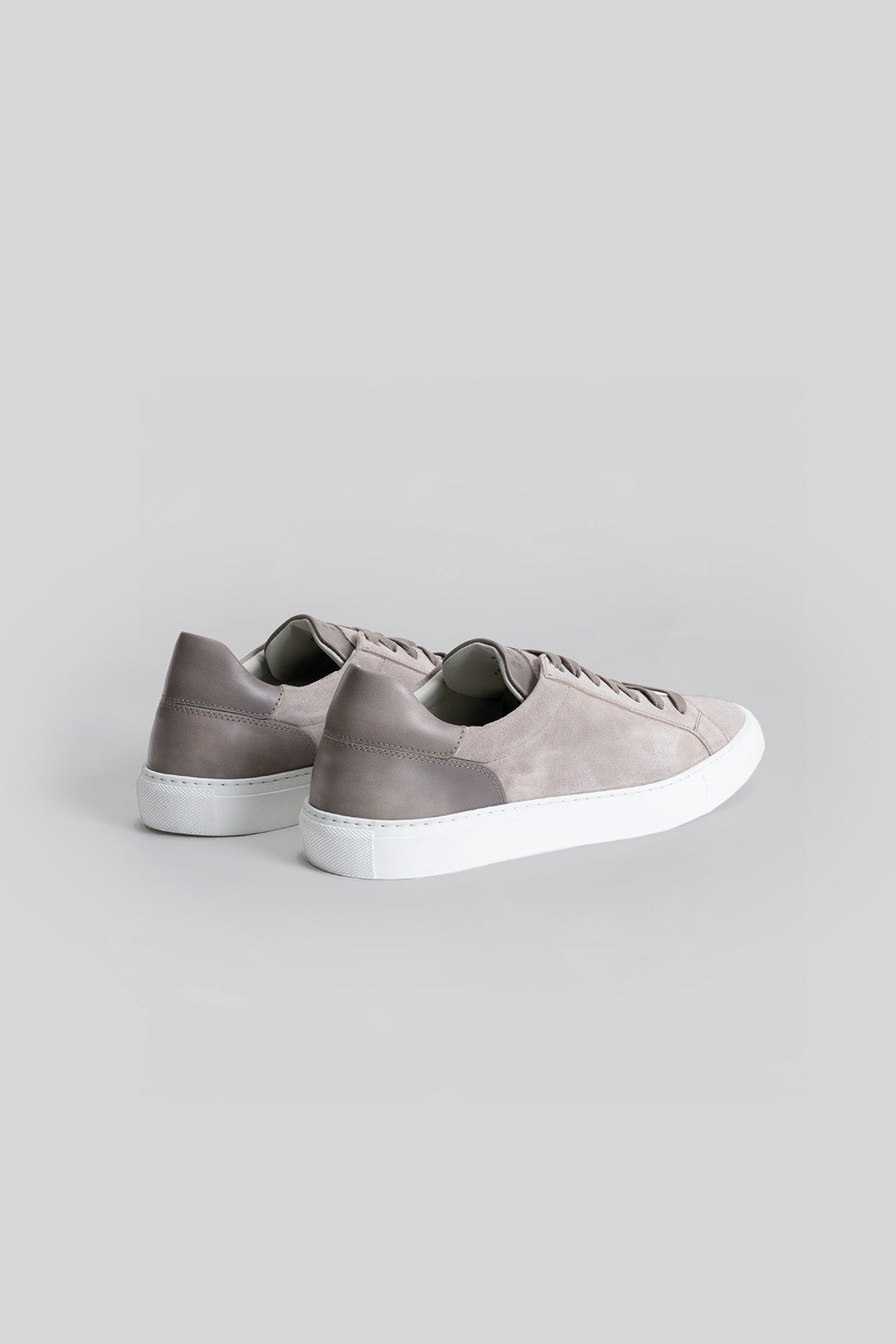 Gray suede sneakers with white rubber sole and lace-up closure, shown from rear three-quarter view.