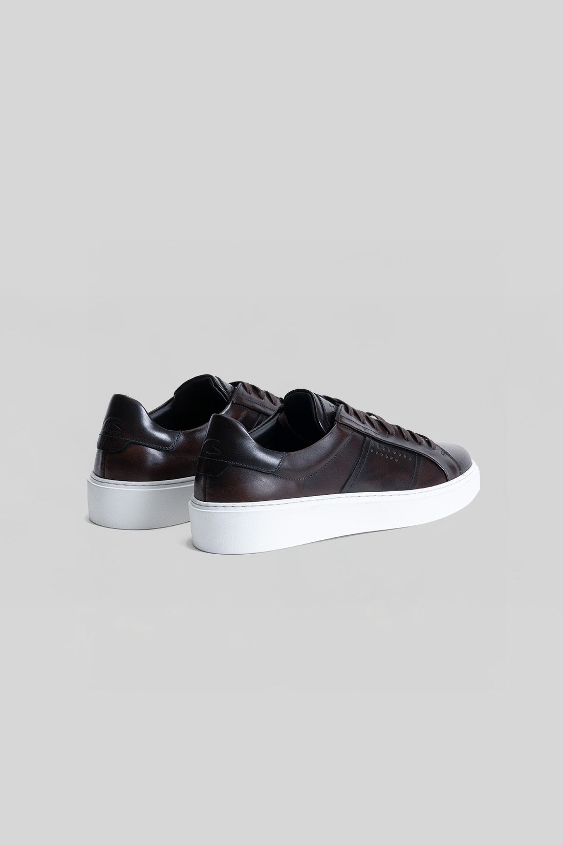 Dark brown leather sneaker with white platform sole, shown from rear three-quarter view.