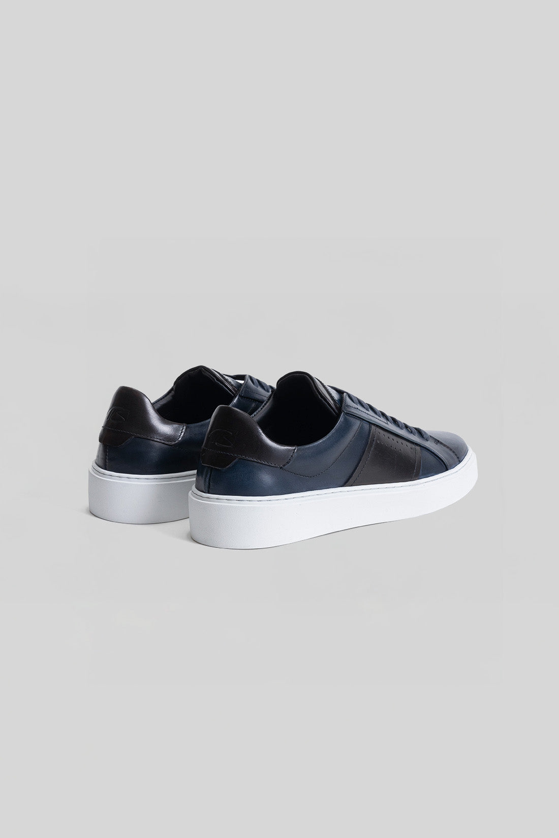 Black leather low-top sneaker with white platform sole, shown from rear three-quarter view.