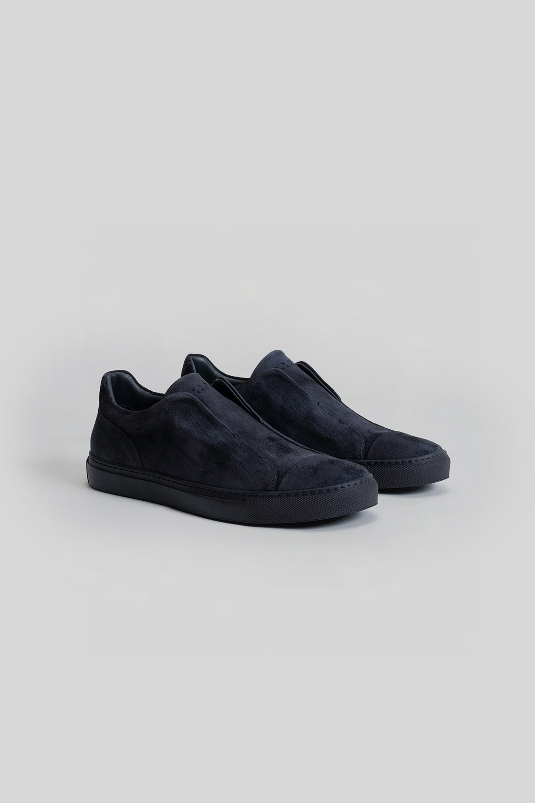 Black suede slip-on sneakers with padded collars and textured rubber soles, shown from an angled side view.
