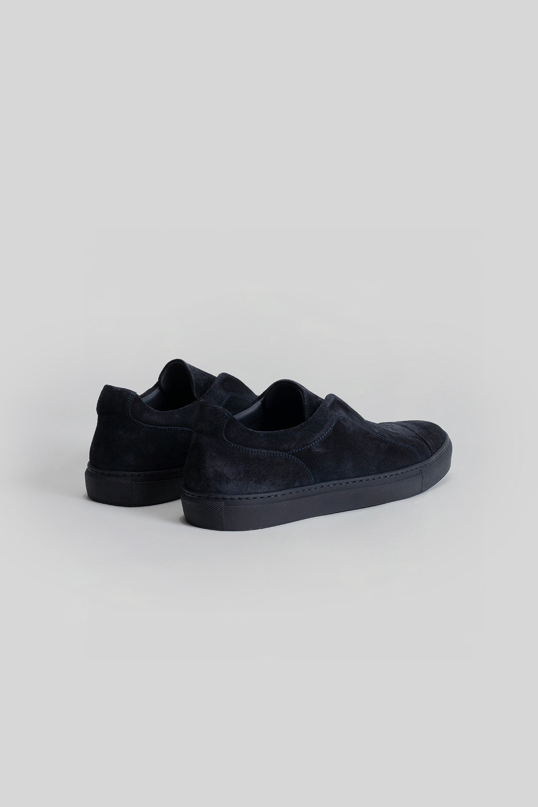 Black suede slip-on sneakers with padded collar and rubber sole, shown from rear angle.