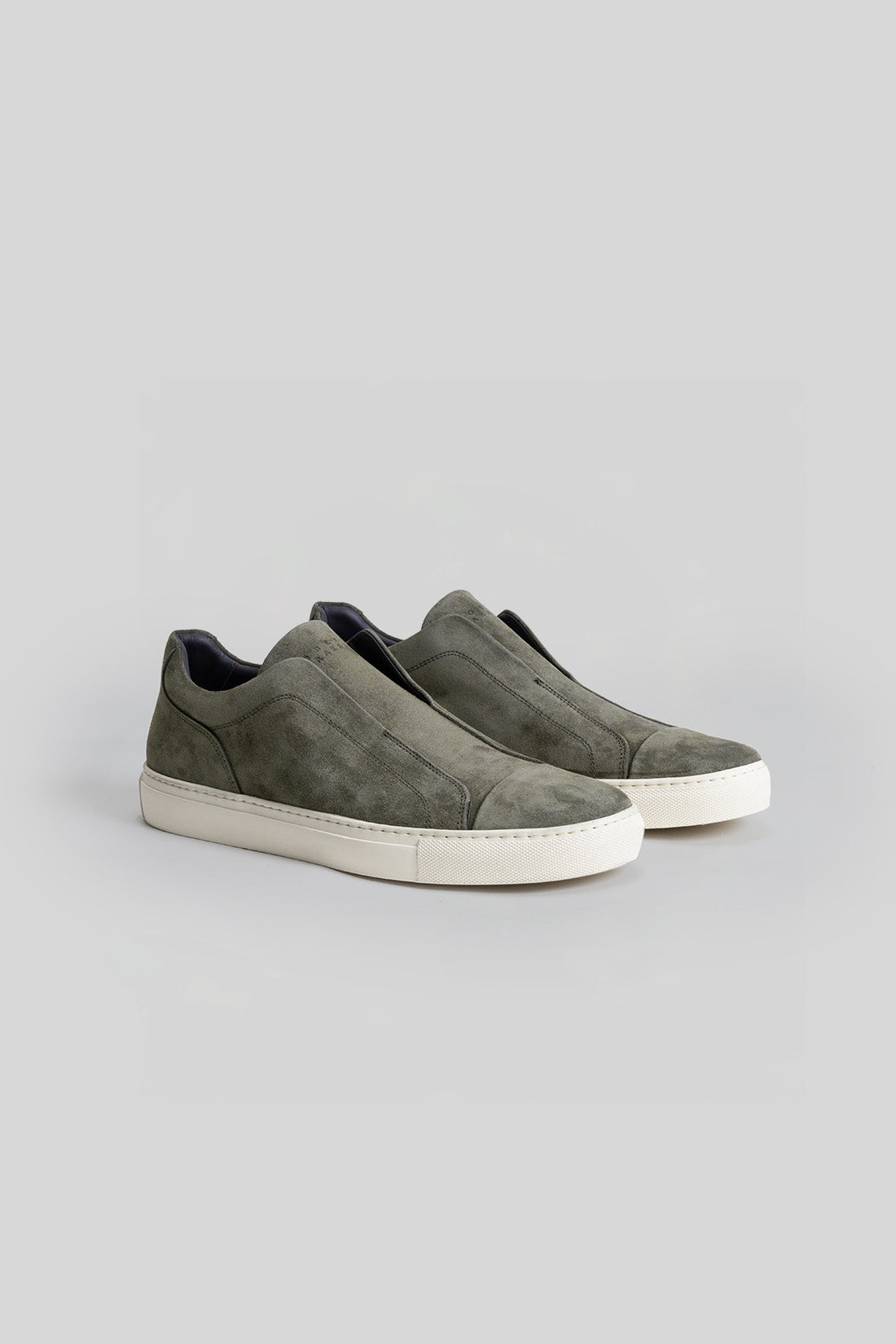Pair of slip-on sneakers in olive suede with white rubber sole and black interior lining.