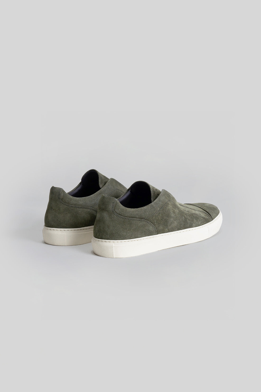 Pair of olive suede slip-on sneakers with white rubber soles, shown from the rear three-quarter view.