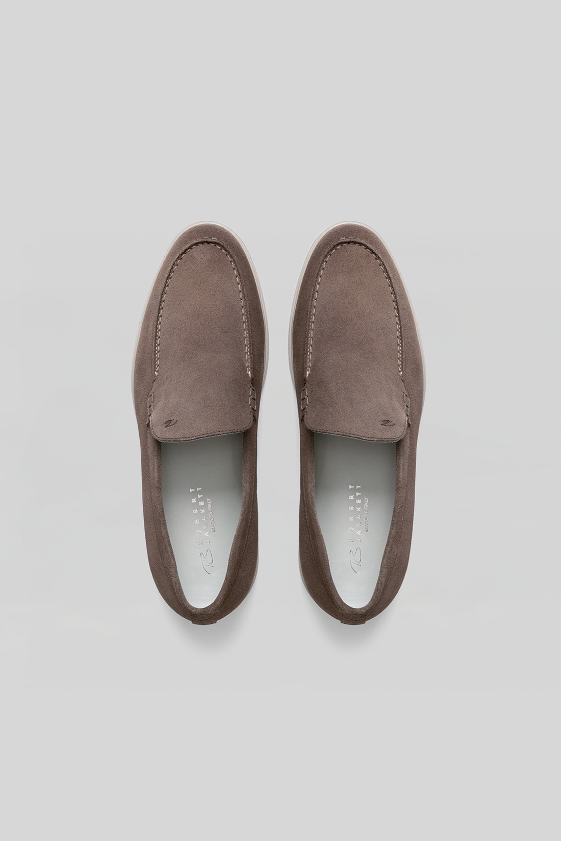 Pair of taupe suede loafers with stitched vamp detail and white leather lining, shown from above.