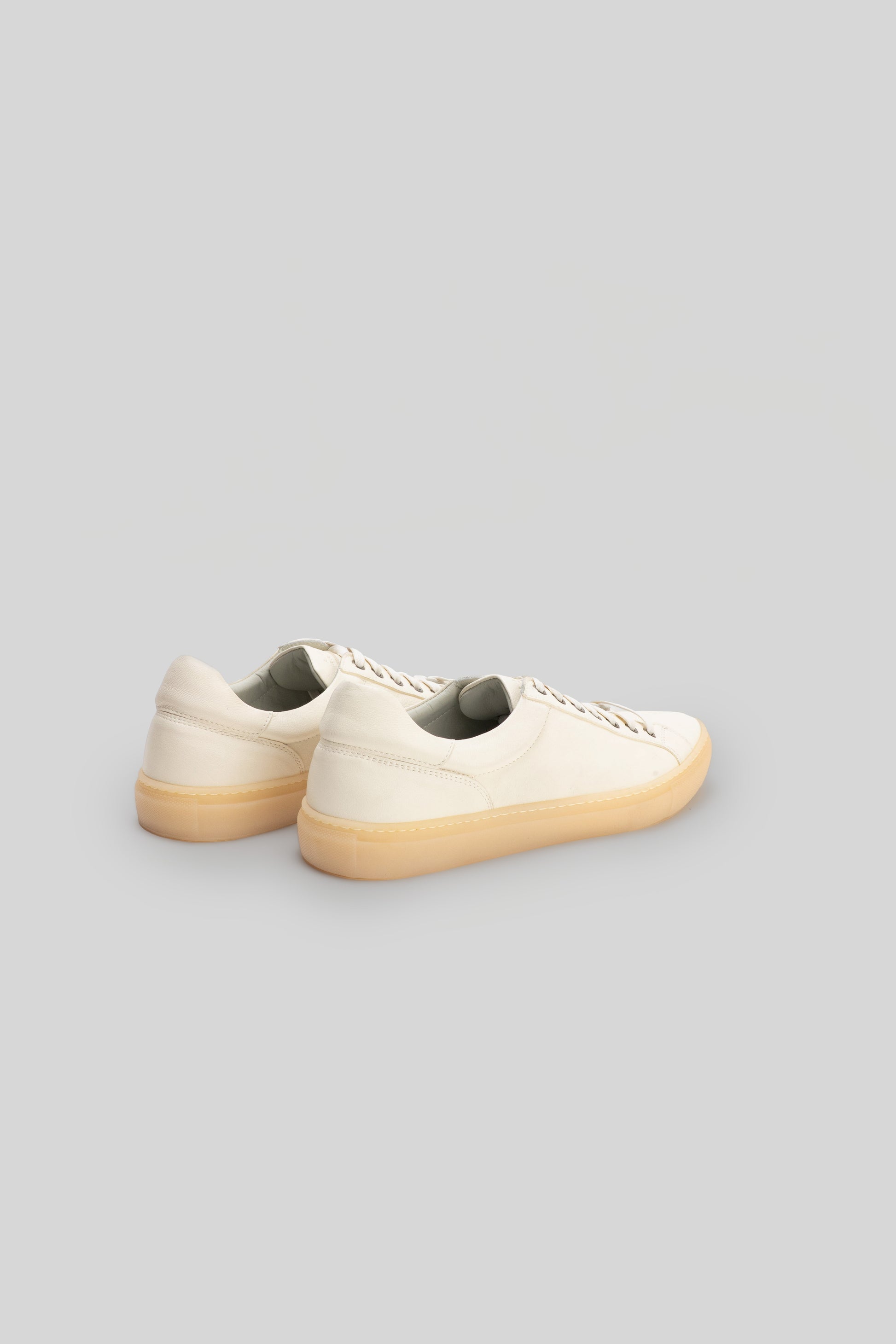 Pair of cream leather sneakers with tan rubber soles, shown from the rear three-quarter view.