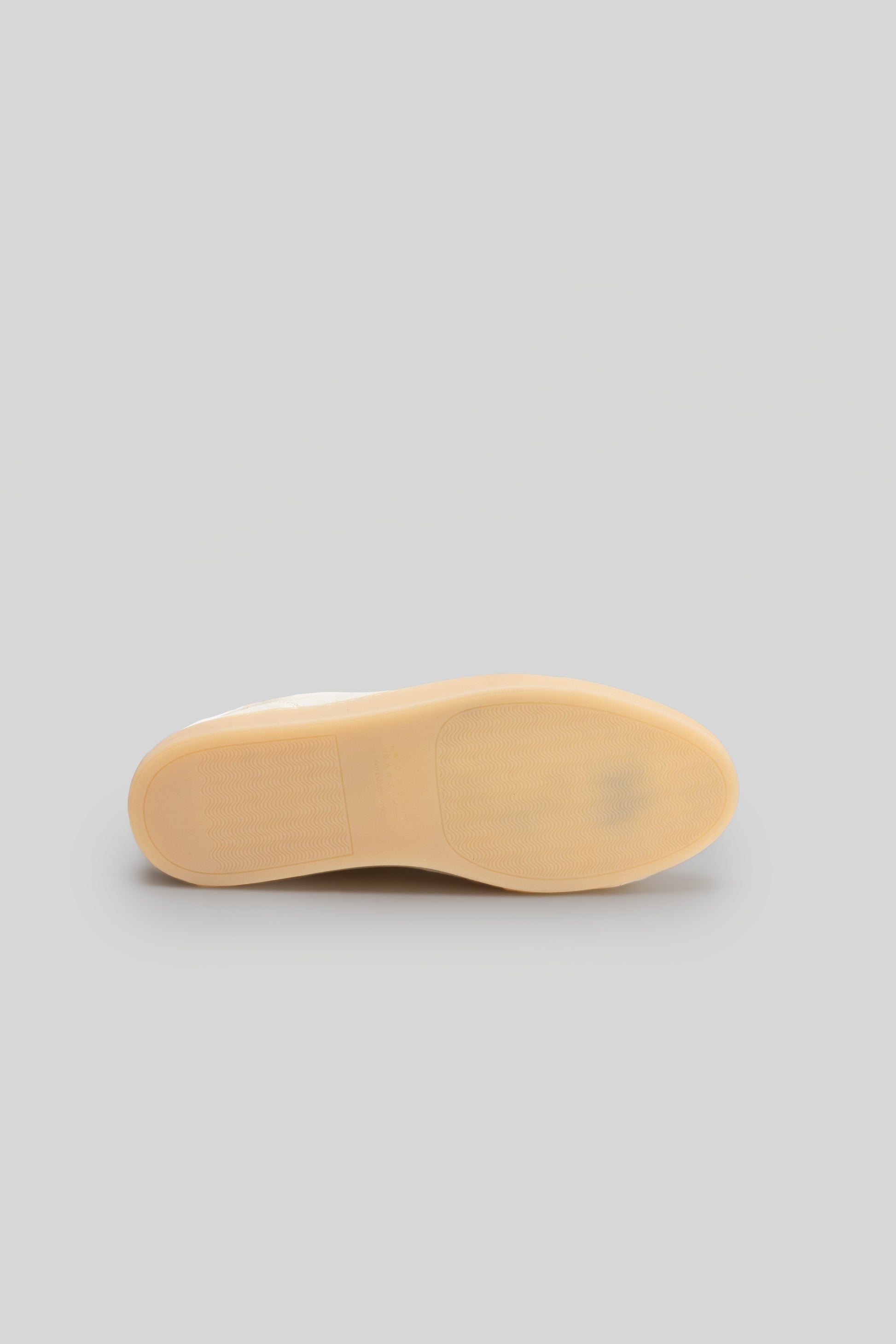 Cream-colored rubber sole of a sneaker with textured tread pattern, shown from underneath.
