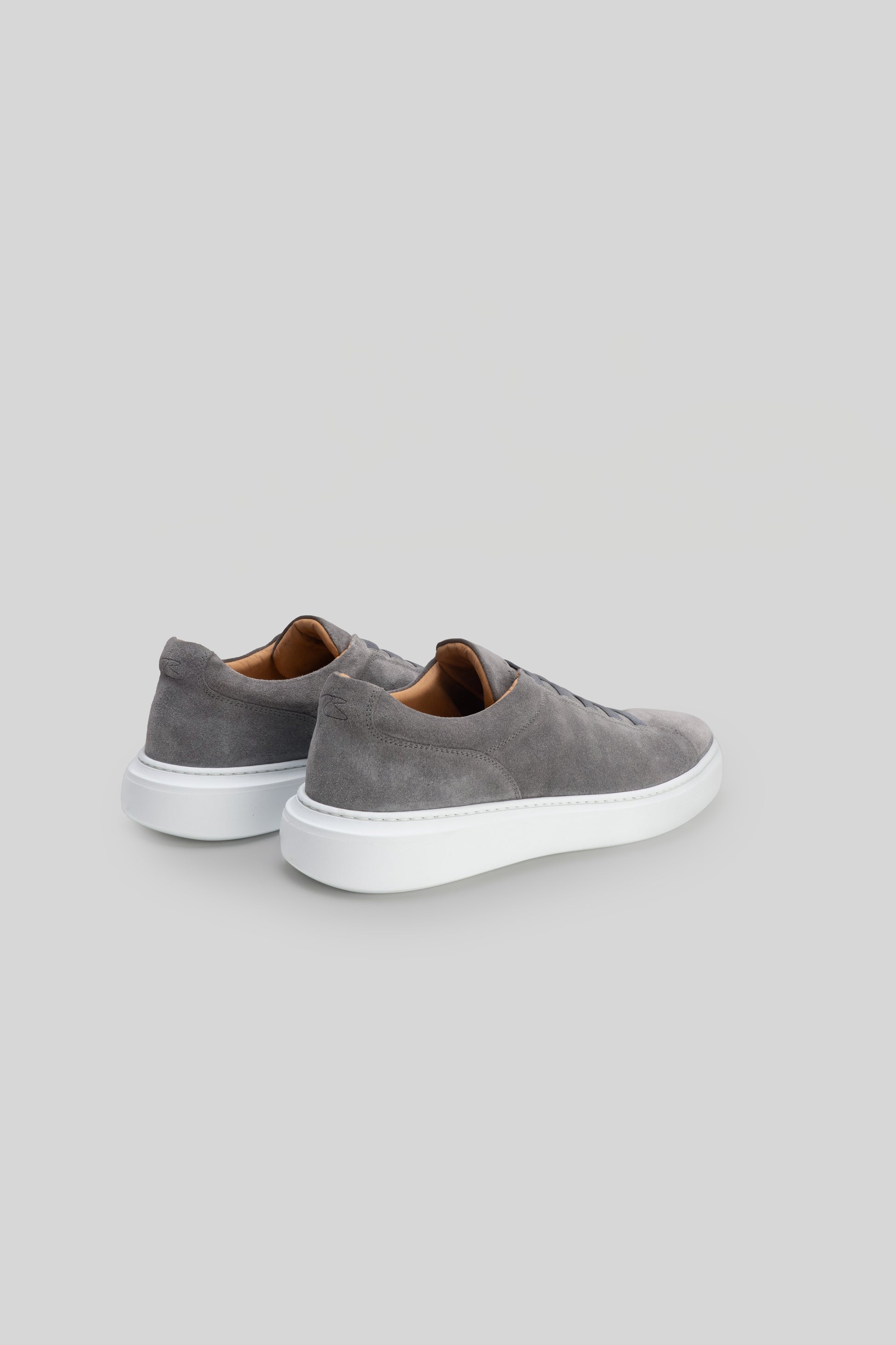 Gray suede slip-on sneakers with white sole and tan interior lining, shown from rear three-quarter view.