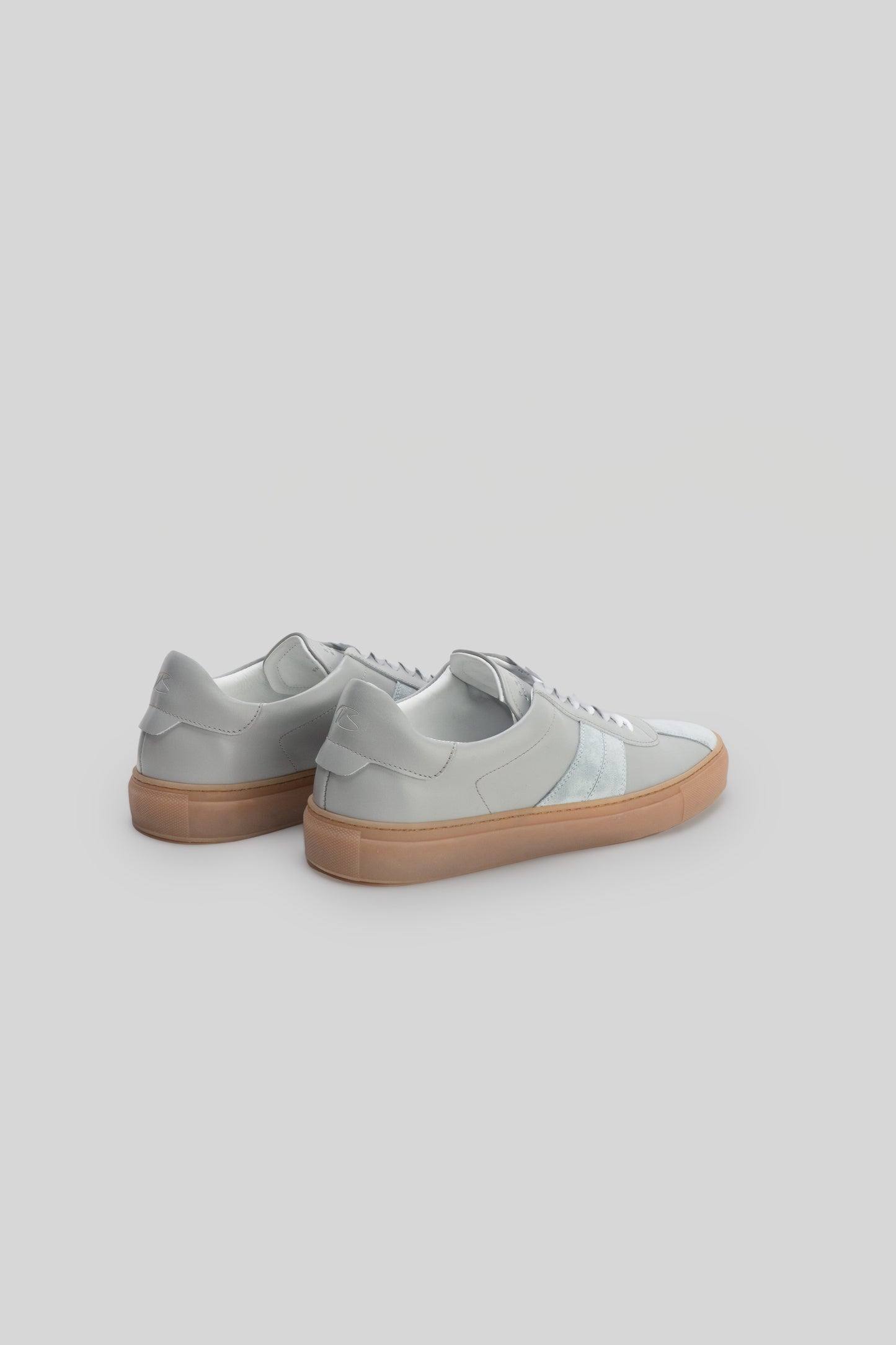 White leather sneakers with tan gum sole, shown from rear three-quarter view.