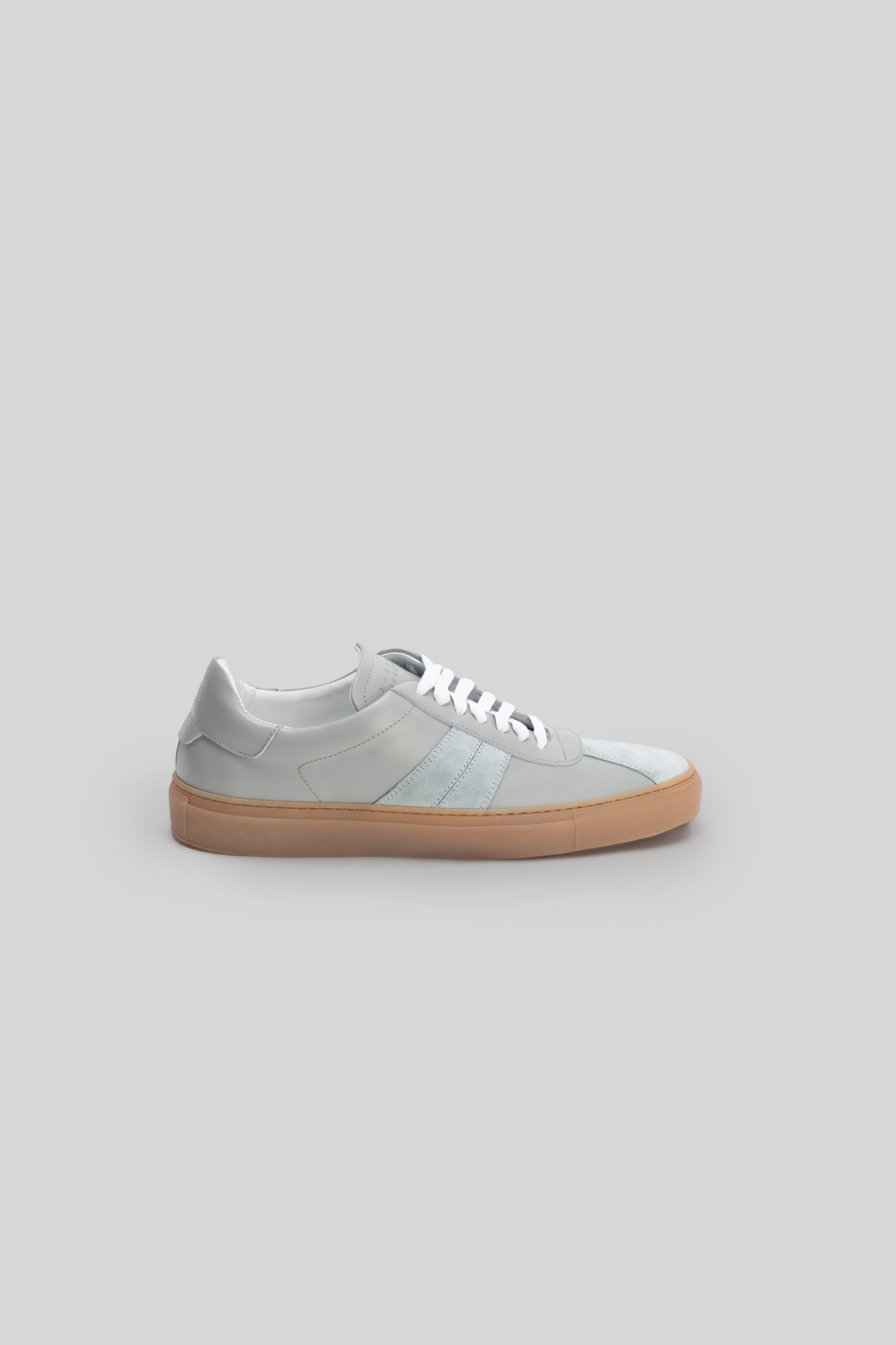 White leather sneaker with horizontal stripe detailing and tan rubber sole, shown in profile view.