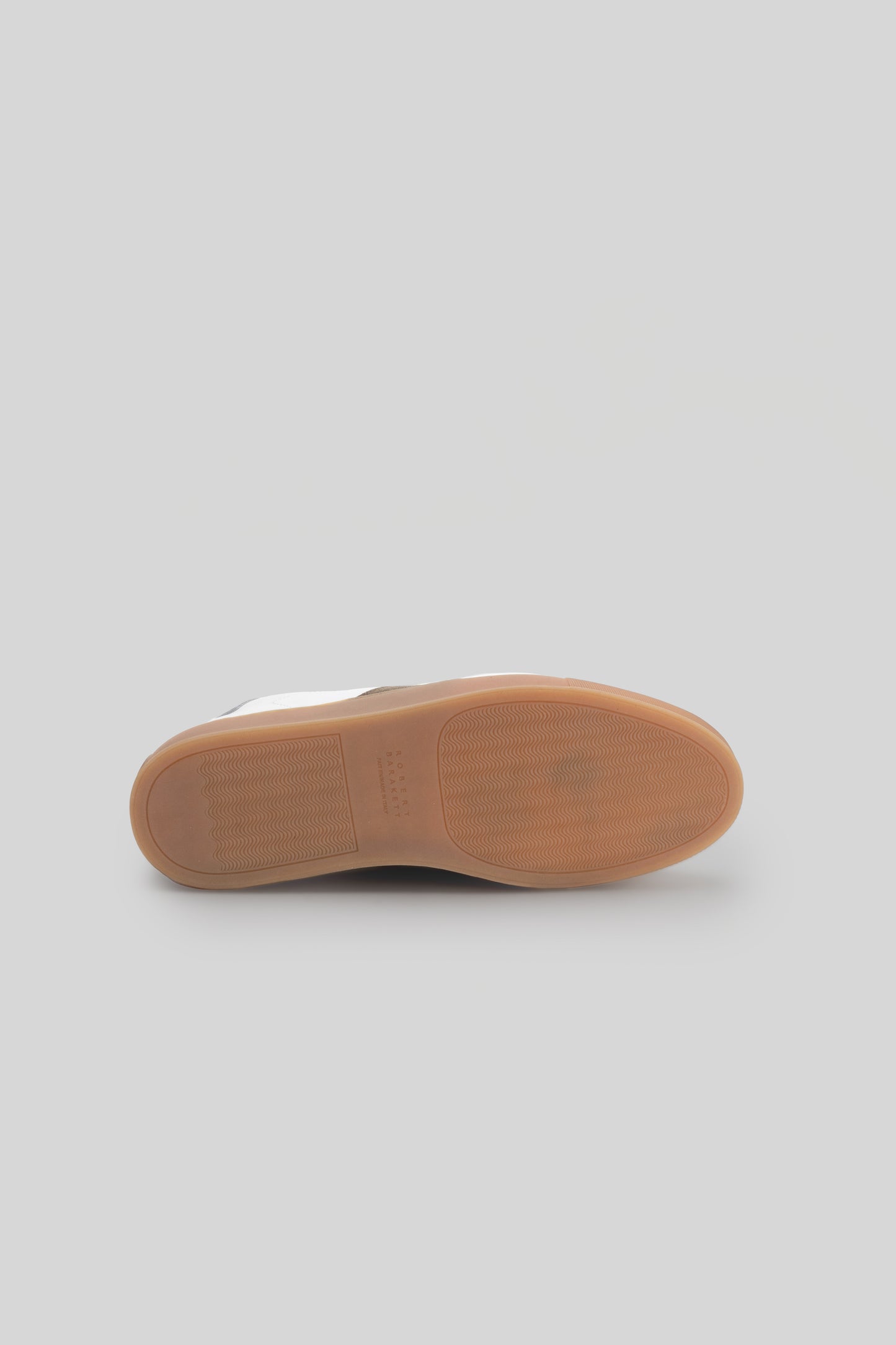 Tan rubber sole with textured tread pattern shown from bottom view of white sneaker.