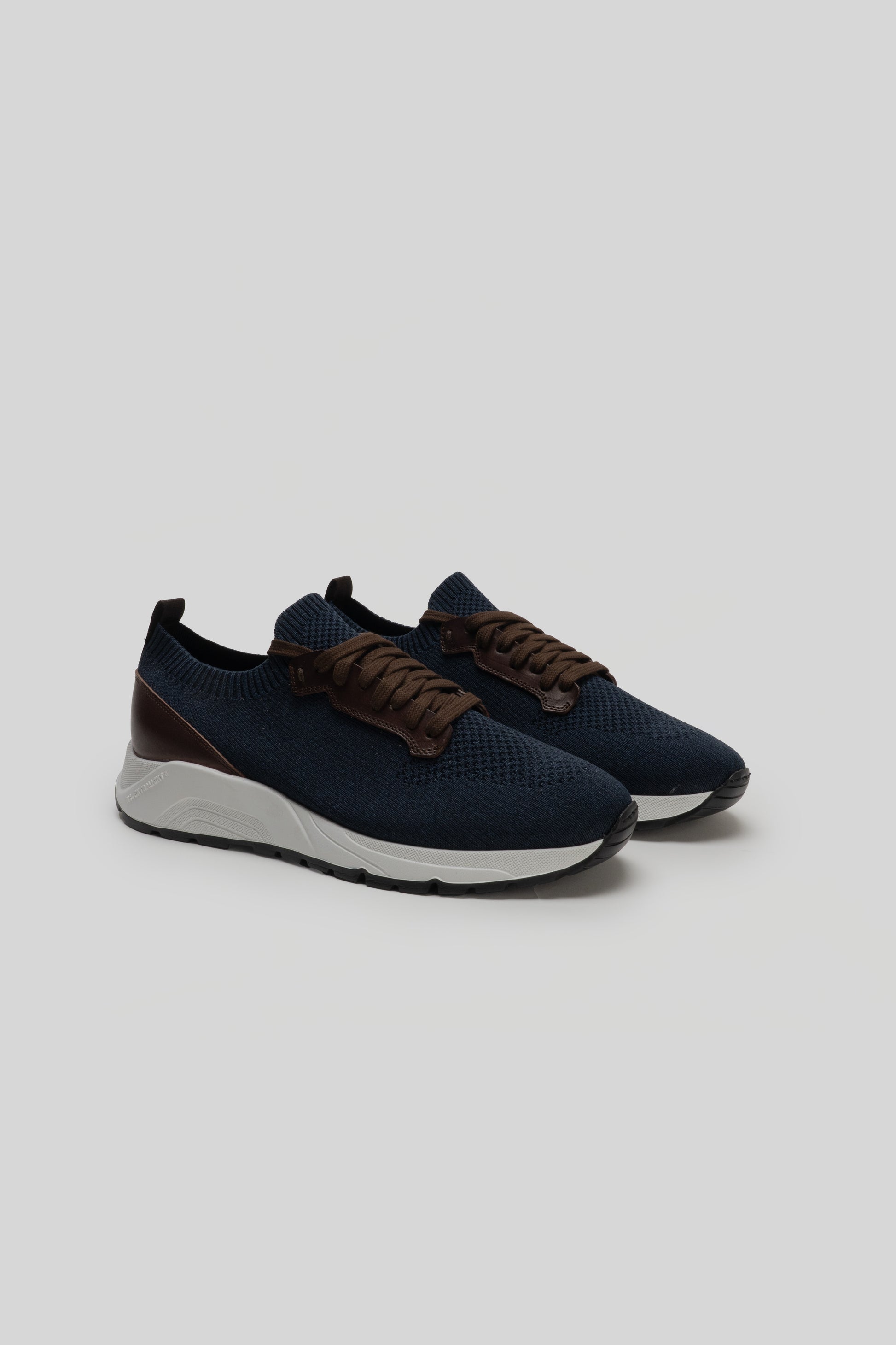Navy knit sneakers with brown leather laces, white midsole, and black heel counter.