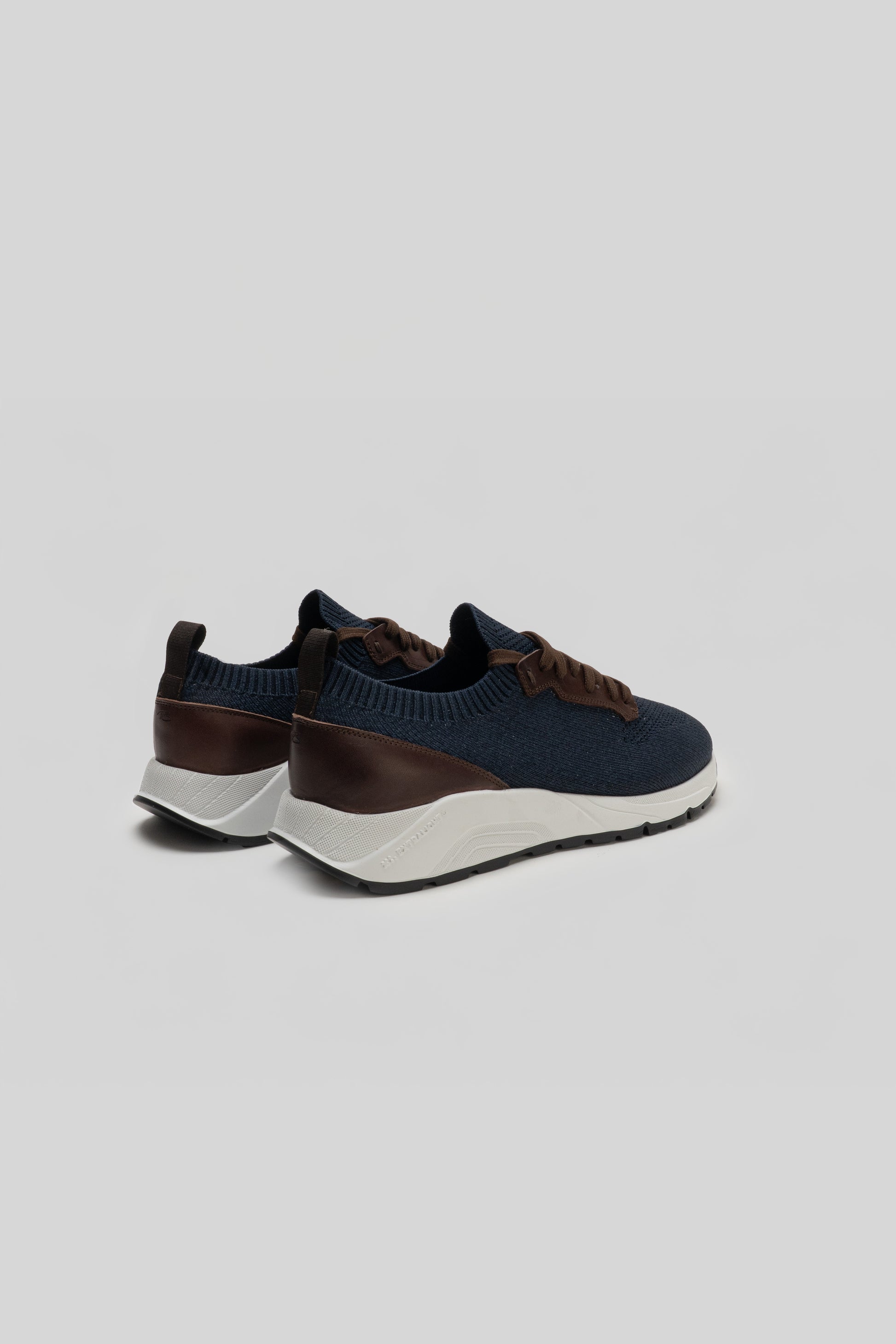 Navy knit sneaker with brown leather heel cup and white sole, shown from the back.
