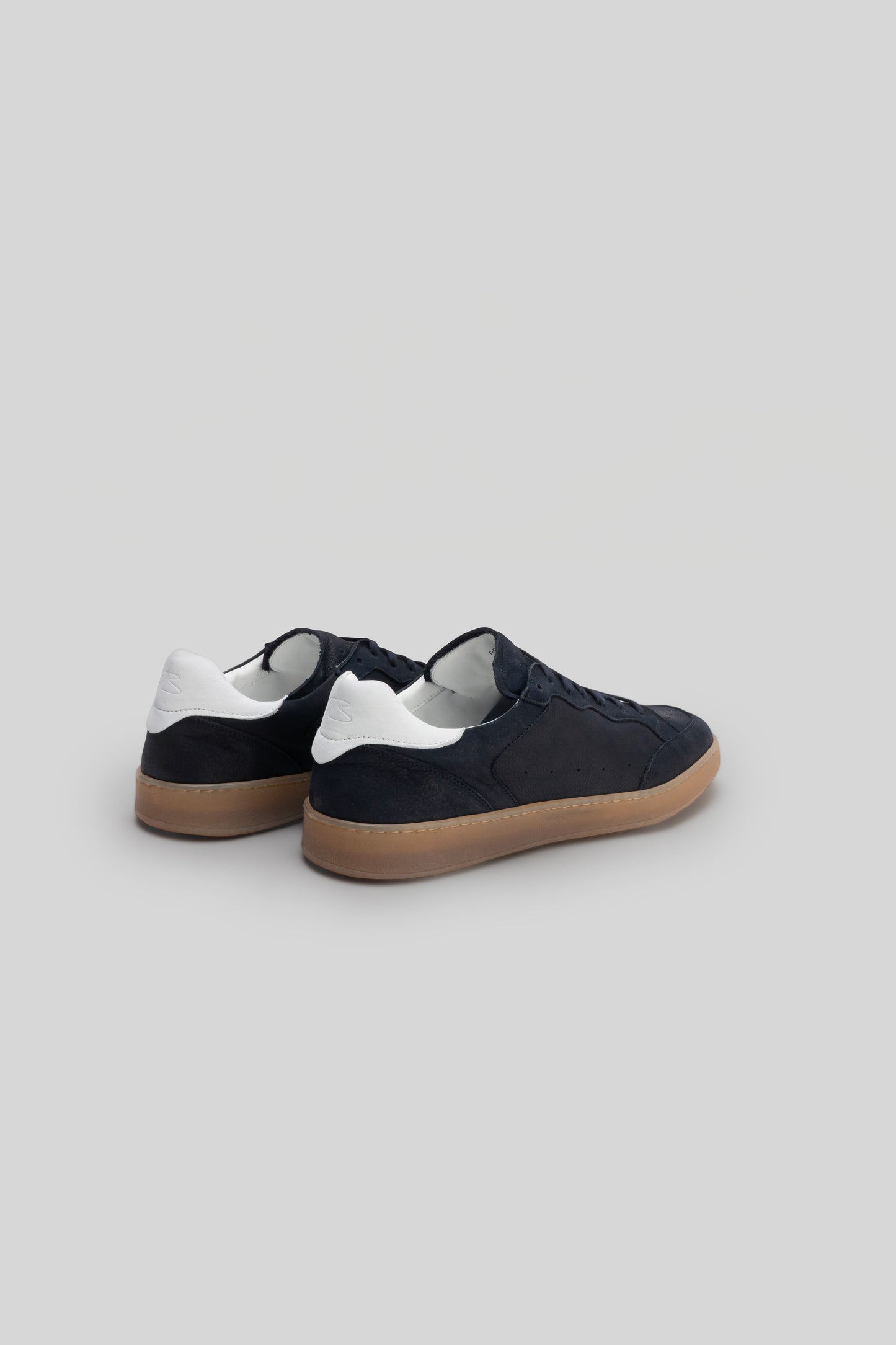 Black and white low-top sneaker with tan rubber sole, shown from rear three-quarter view.