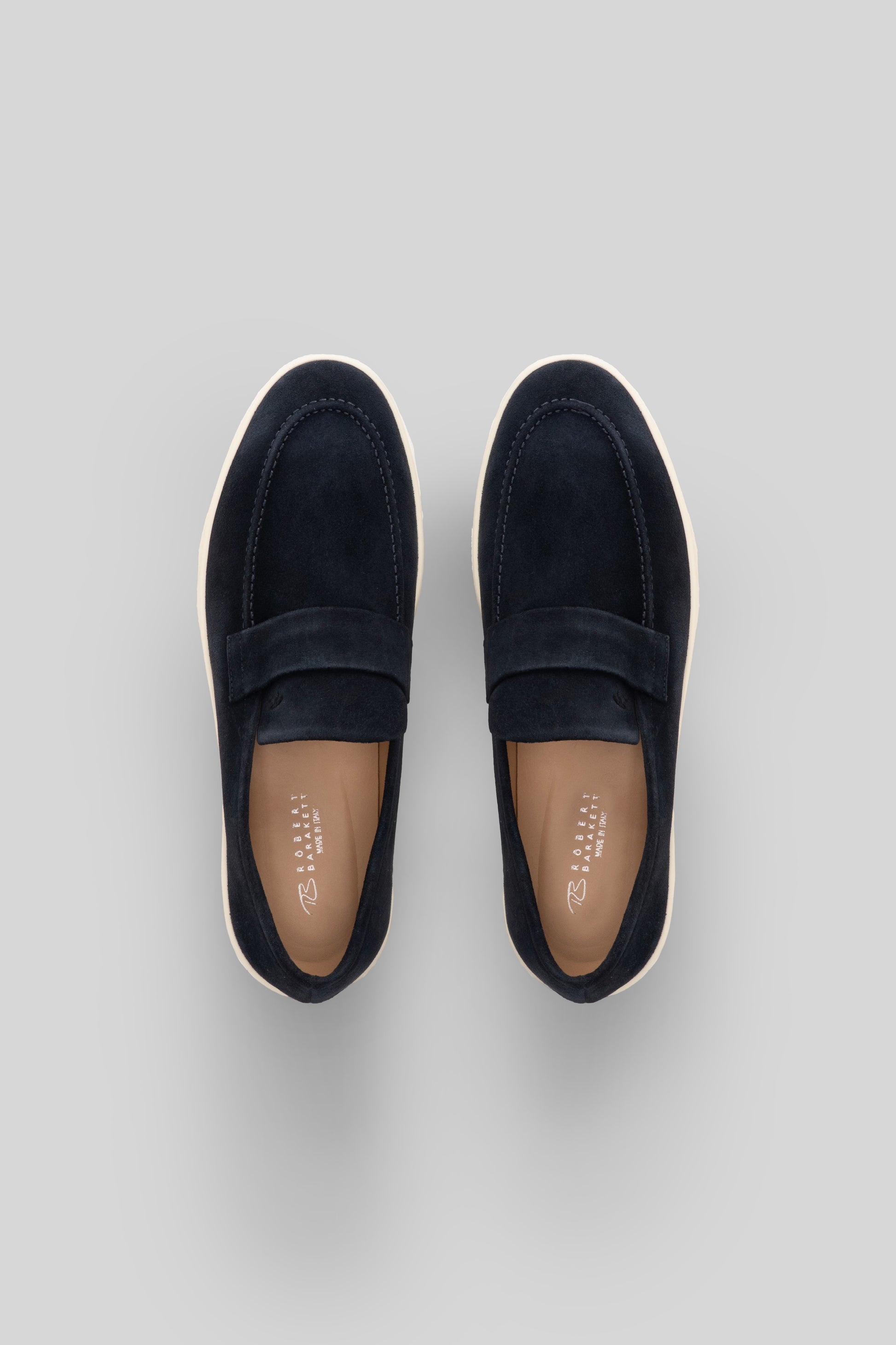 Navy suede loafer-style sneaker with cream rubber sole, shown from above.