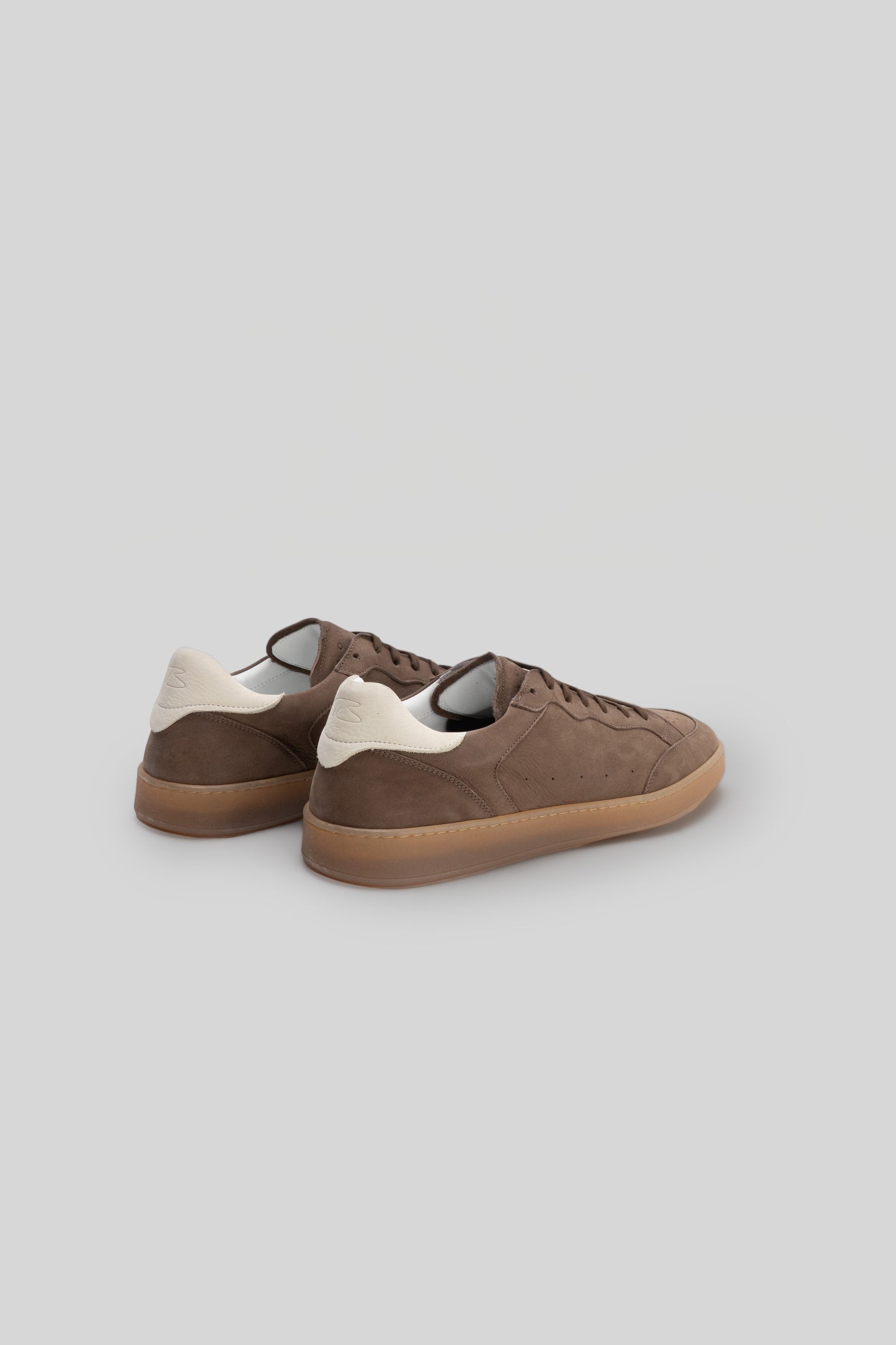 Brown suede sneaker with cream heel tab and gum sole, shown from rear three-quarter view.