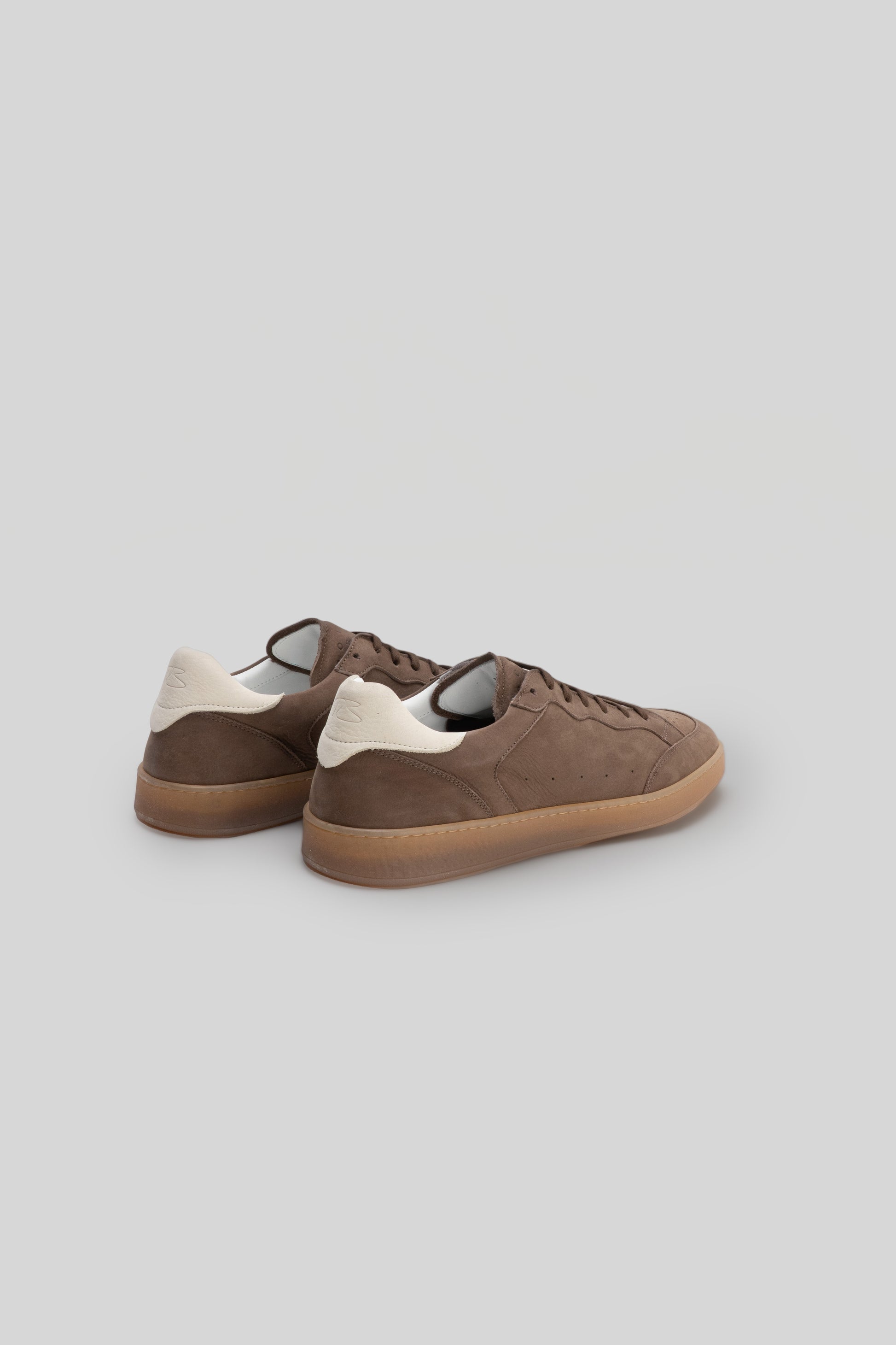 Brown suede sneaker with cream heel tab and gum sole, shown from rear three-quarter view.