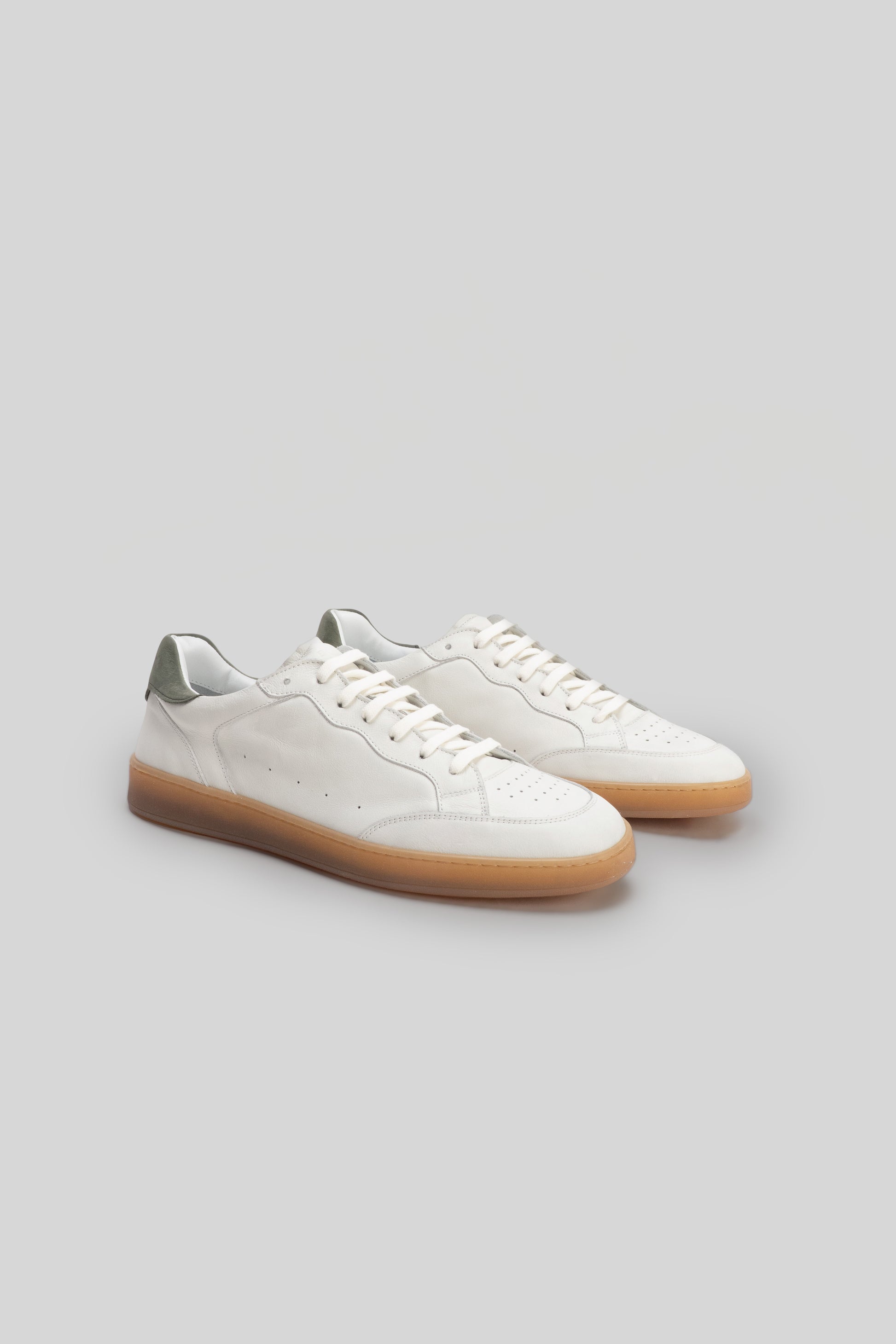 White leather low-top sneaker with gum sole and sage green heel counter, shown from a three-quarter view.
