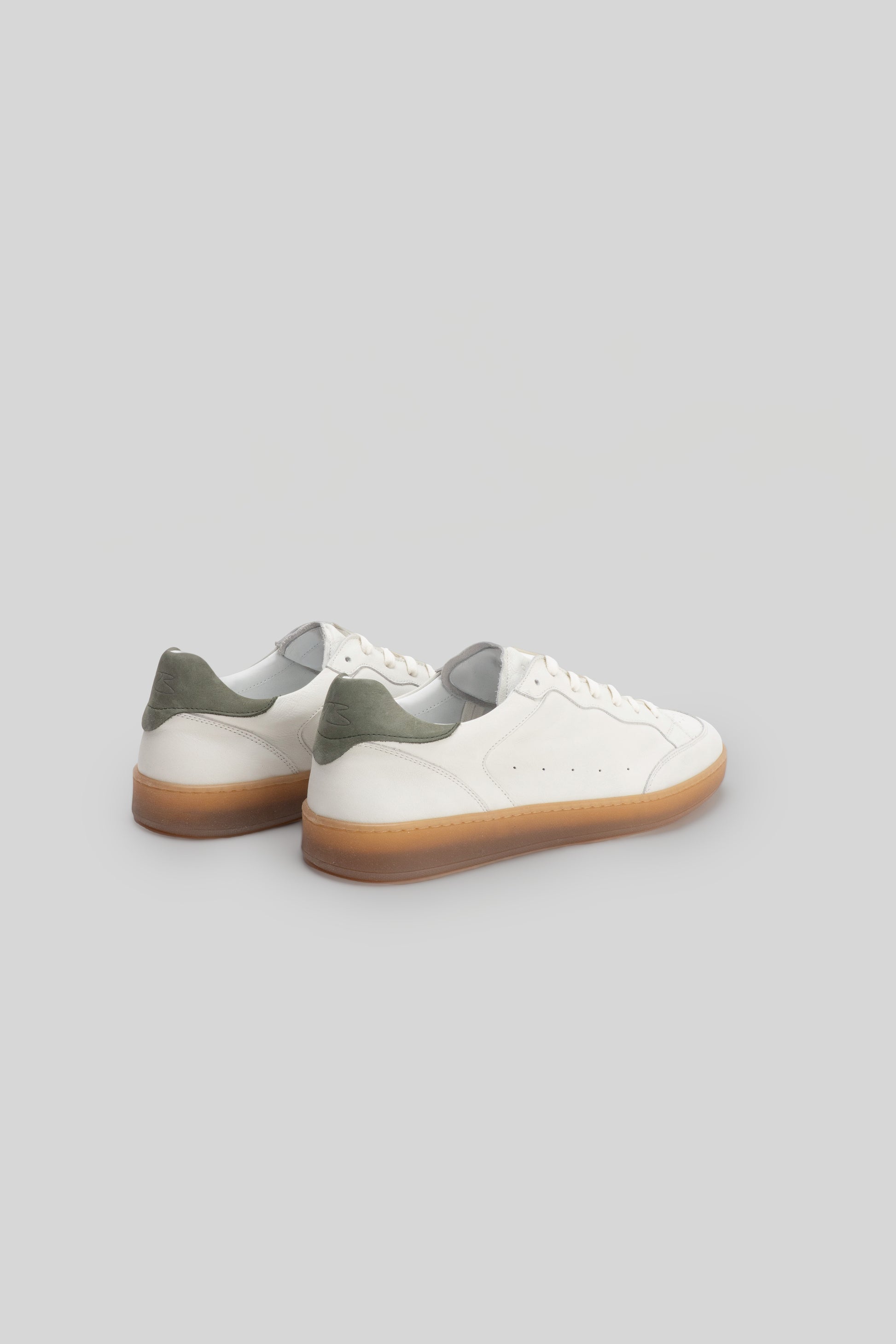 White leather sneakers with olive green heel tabs and gum rubber sole, shown from rear three-quarter view.