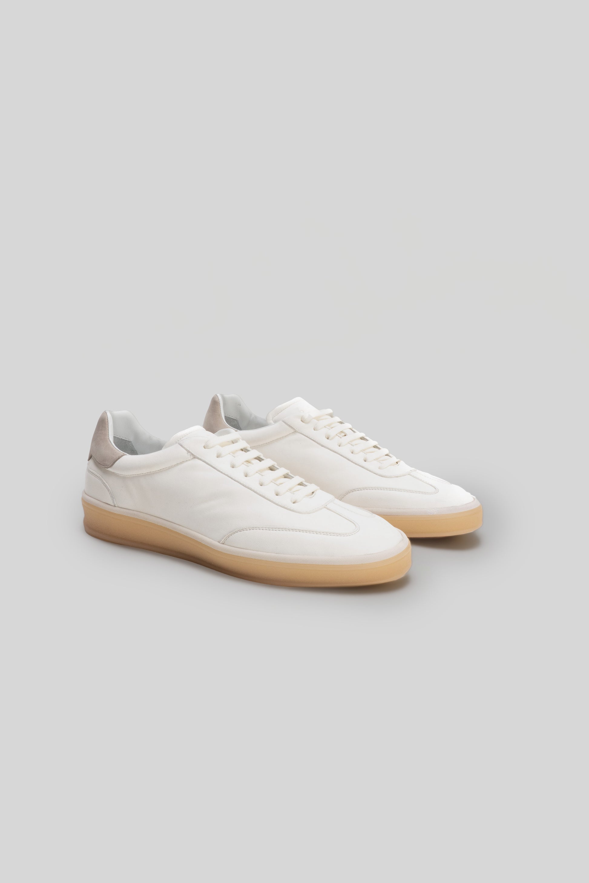 White leather sneakers with tan gum soles, white laces, and padded cream-colored heel collar.
