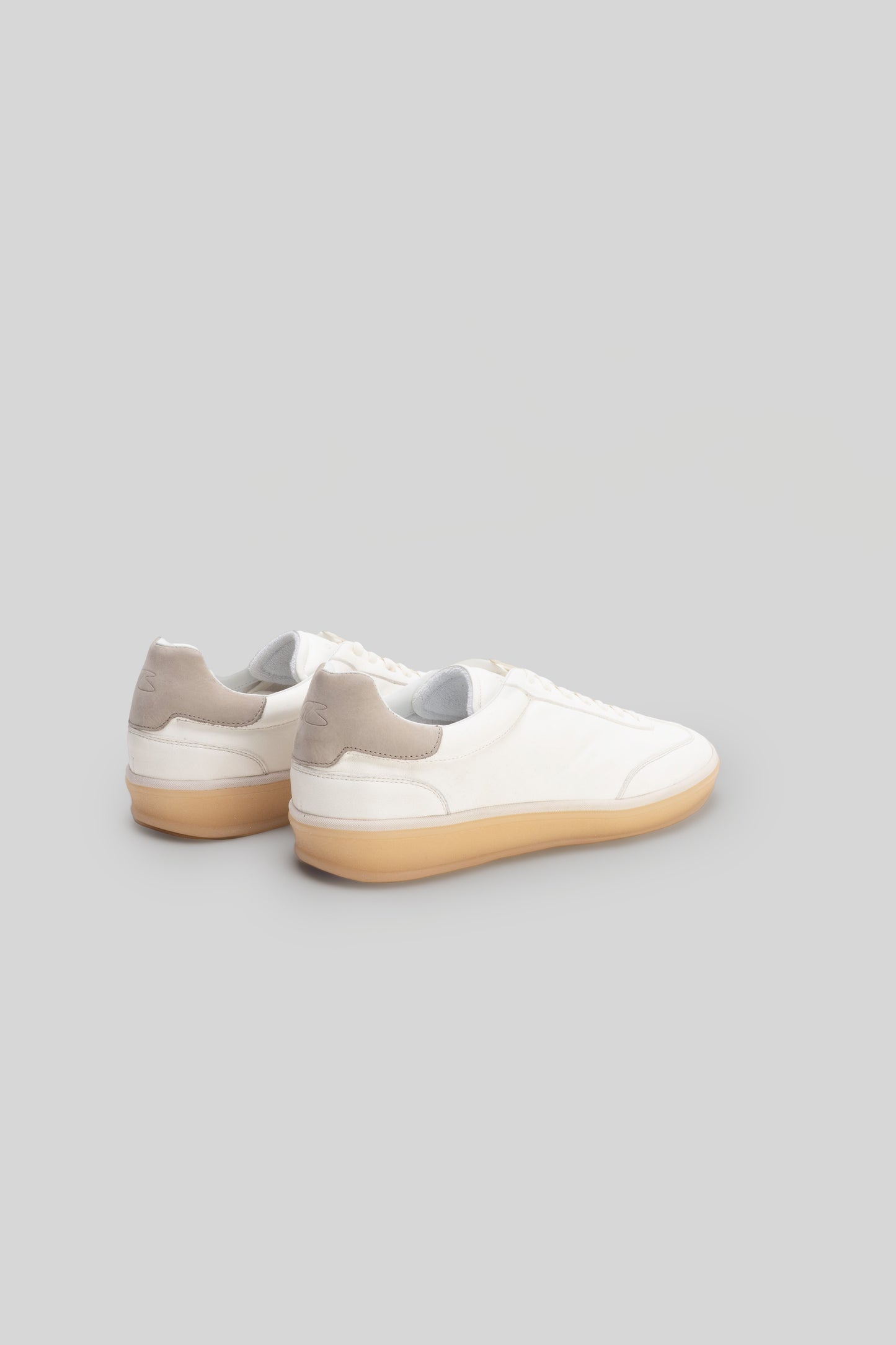 White sneaker with beige heel collar and tan rubber sole, shown from rear three-quarter angle.