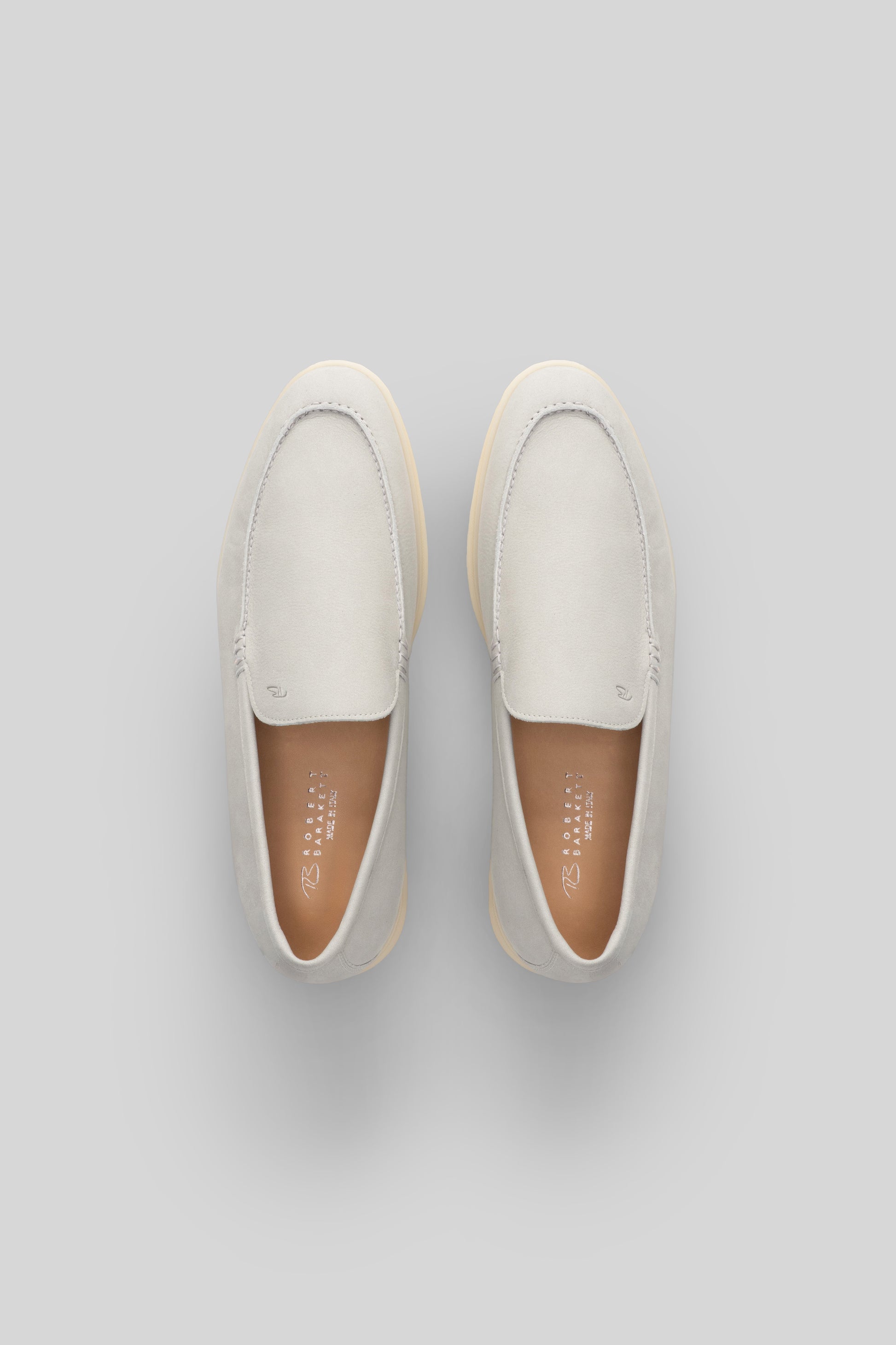 Pair of white suede loafers with tan rubber sole and brown leather insole, shown from above.