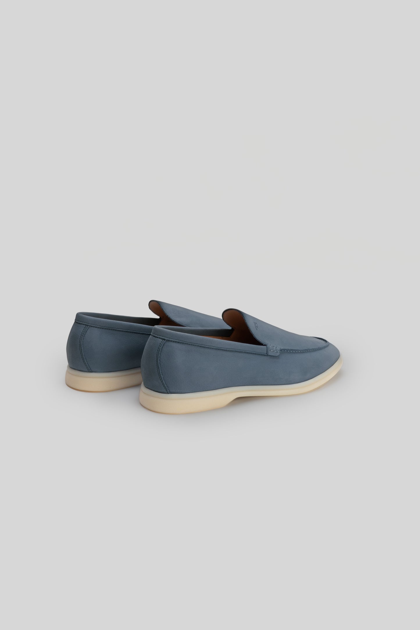 Blue suede loafers with brown leather trim and cream-colored crepe sole, shown from rear three-quarter view.
