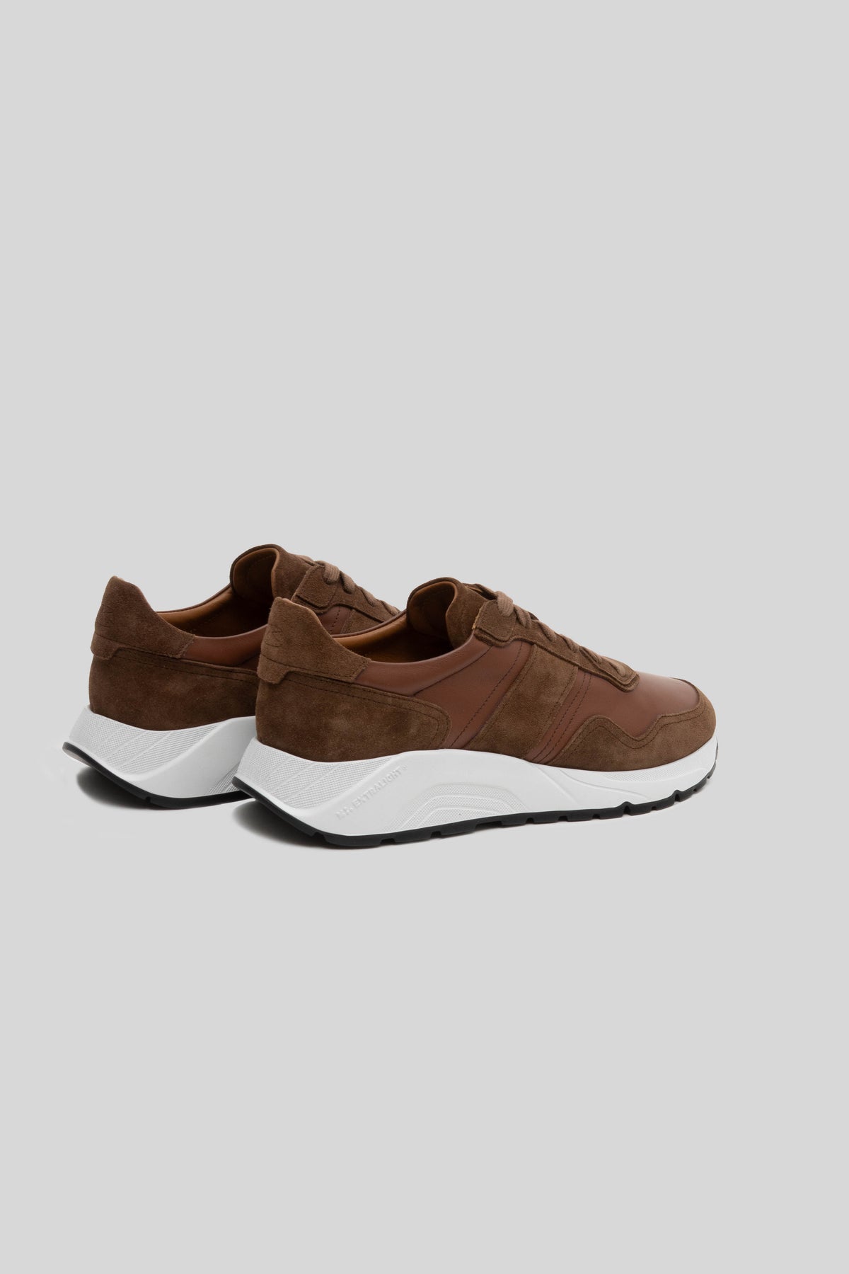 Brown leather and suede sneaker with white and black sole, shown from rear three-quarter view.