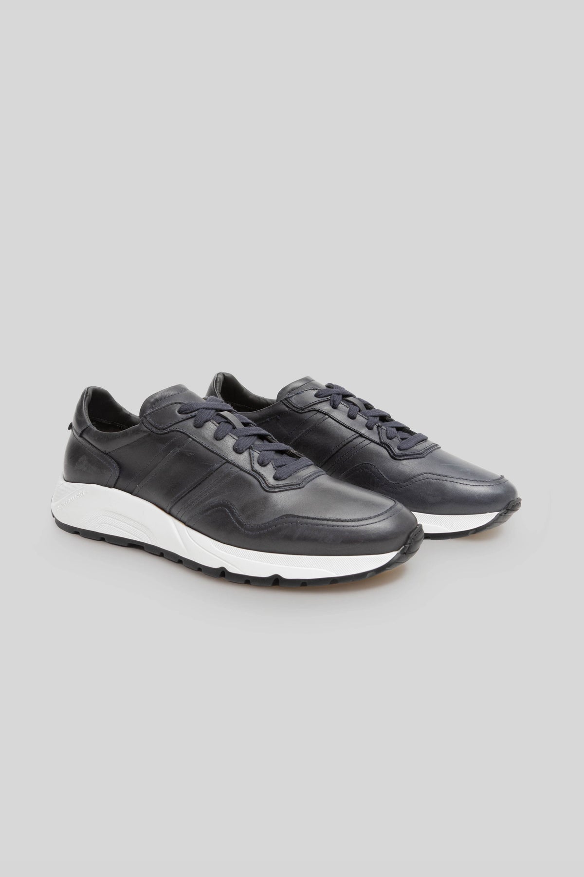 Black leather sneaker with white chunky sole and navy lace closure, shown from three-quarter view.