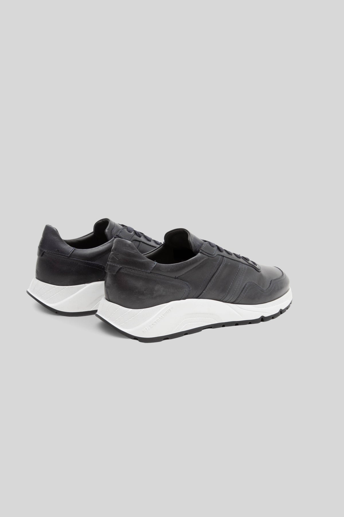 Black leather sneakers with white sole and black trim, shown from rear three-quarter view.