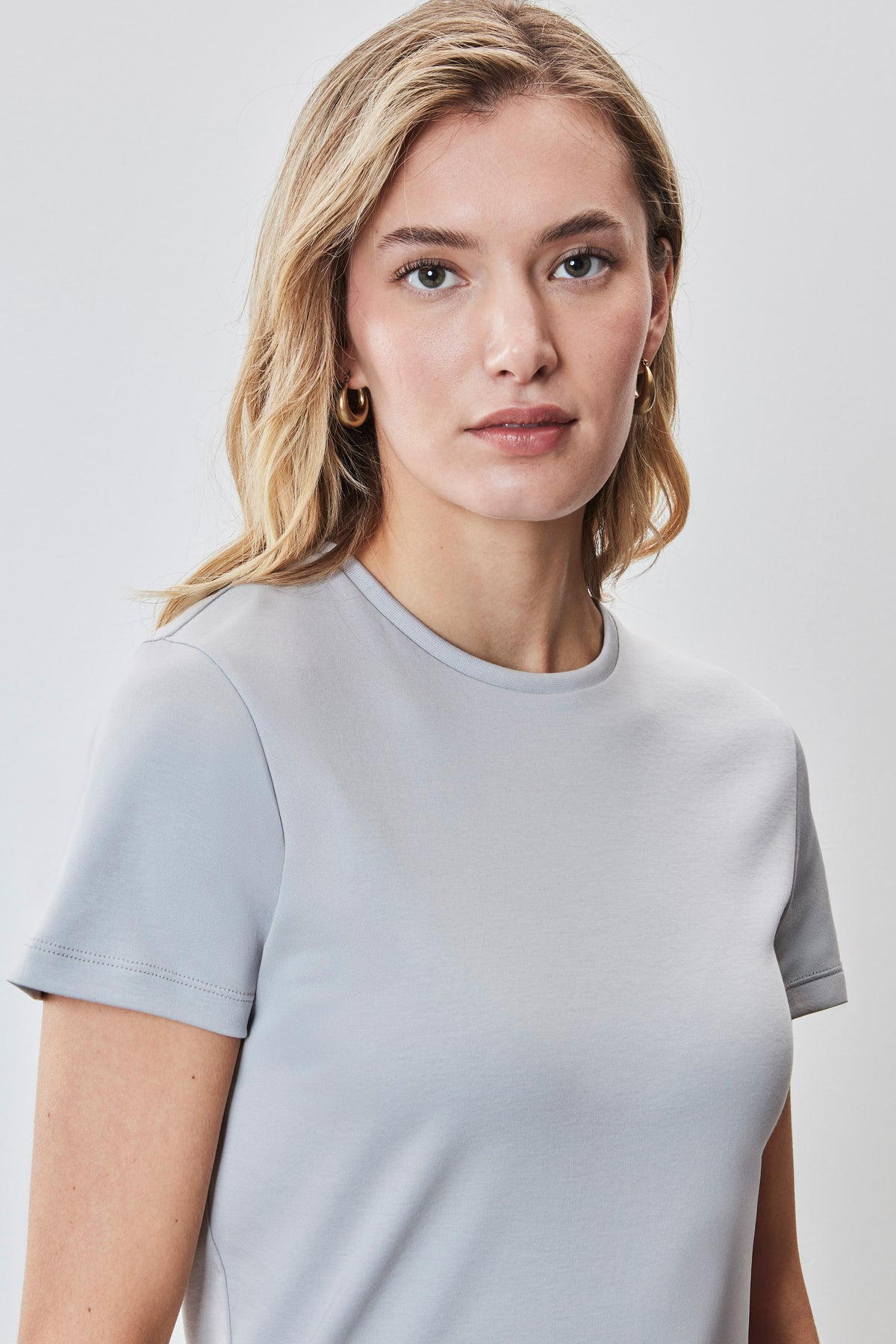 Woman wearing a light gray crew neck t-shirt with short sleeves against a white background.