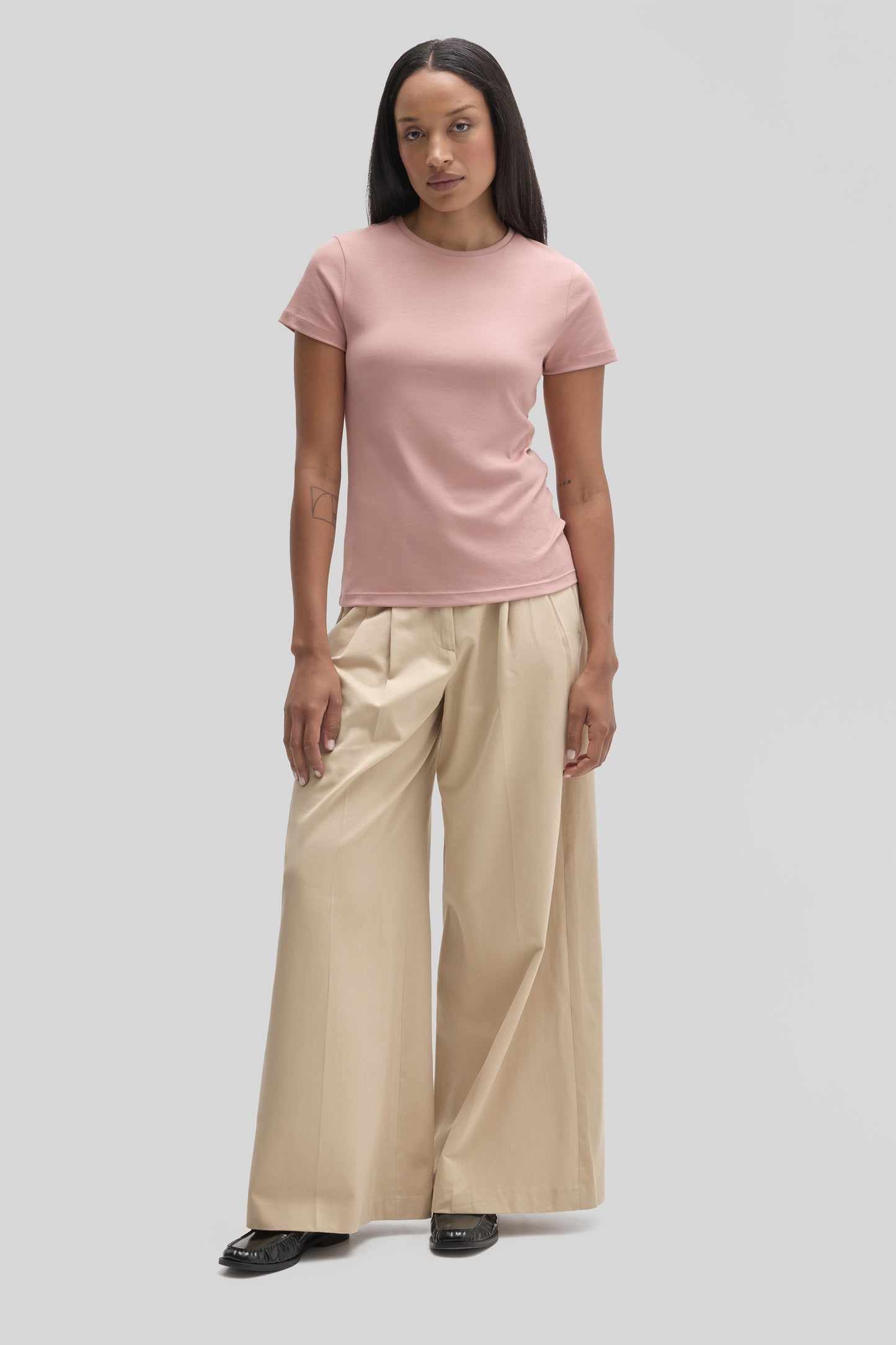 Woman wearing a pink crew neck short-sleeve tee with beige wide-leg pants and black shoes.
