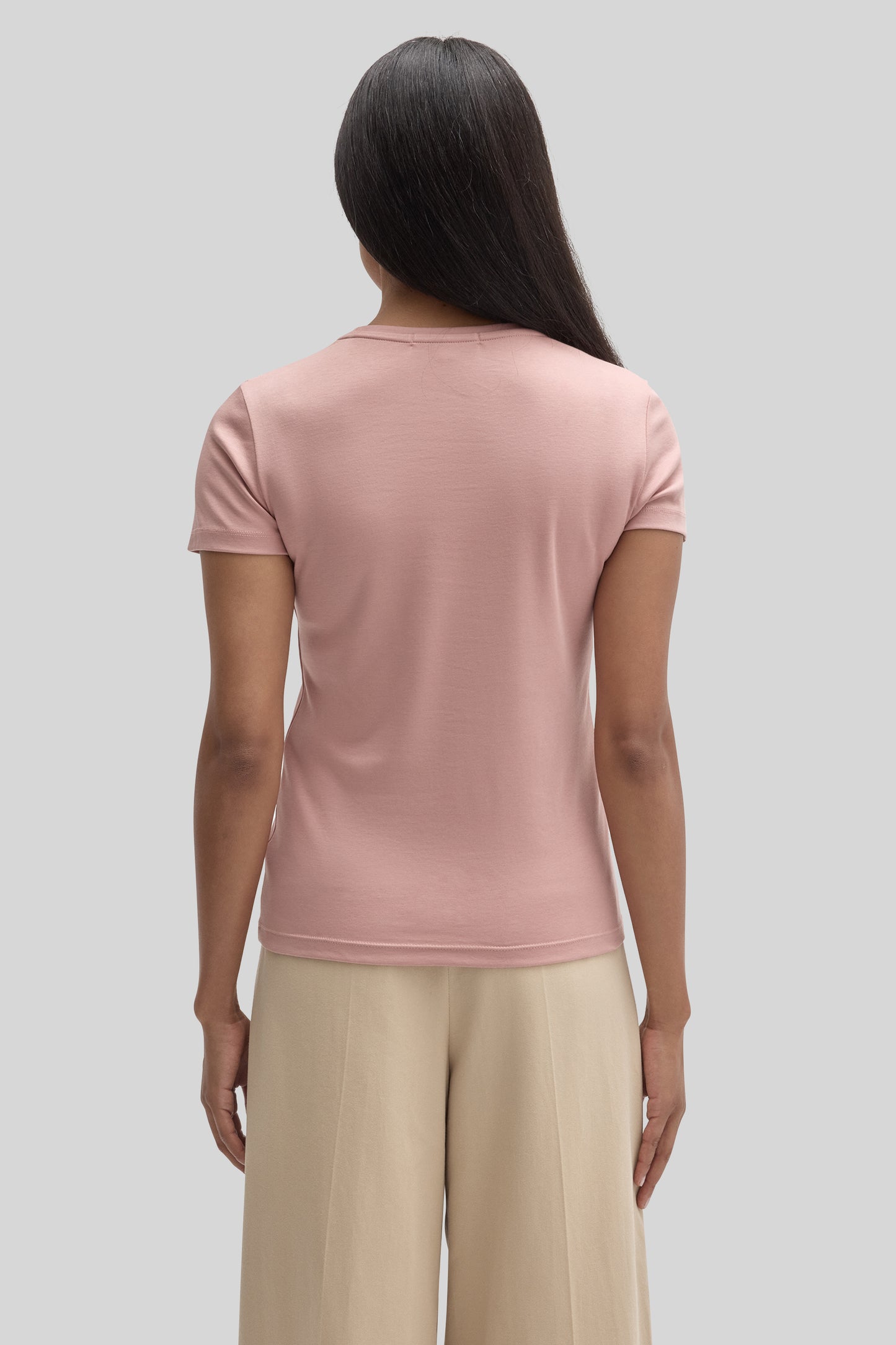 Woman wearing a dusty pink short-sleeve crew neck tee paired with cream-colored trousers, shown from behind.