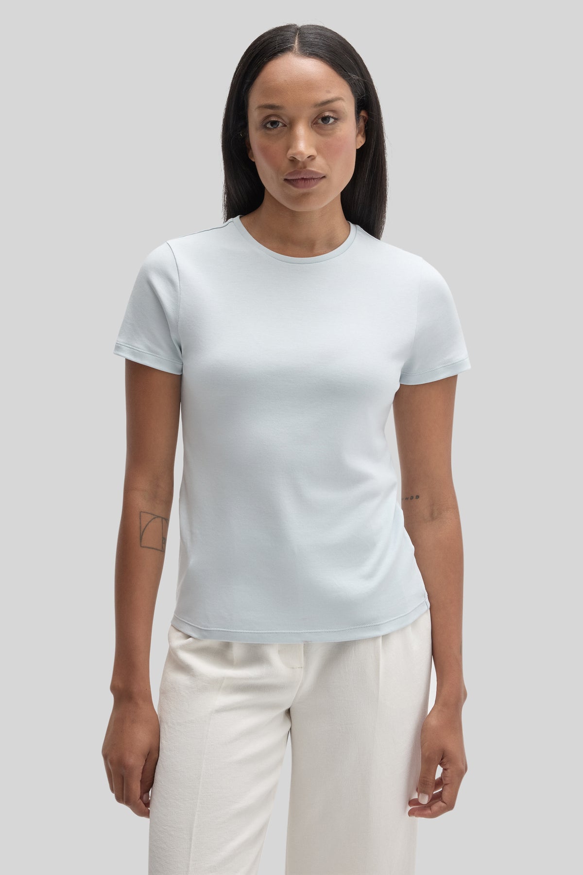 Woman wearing white short-sleeve crew neck tee with cream pants against gray background.