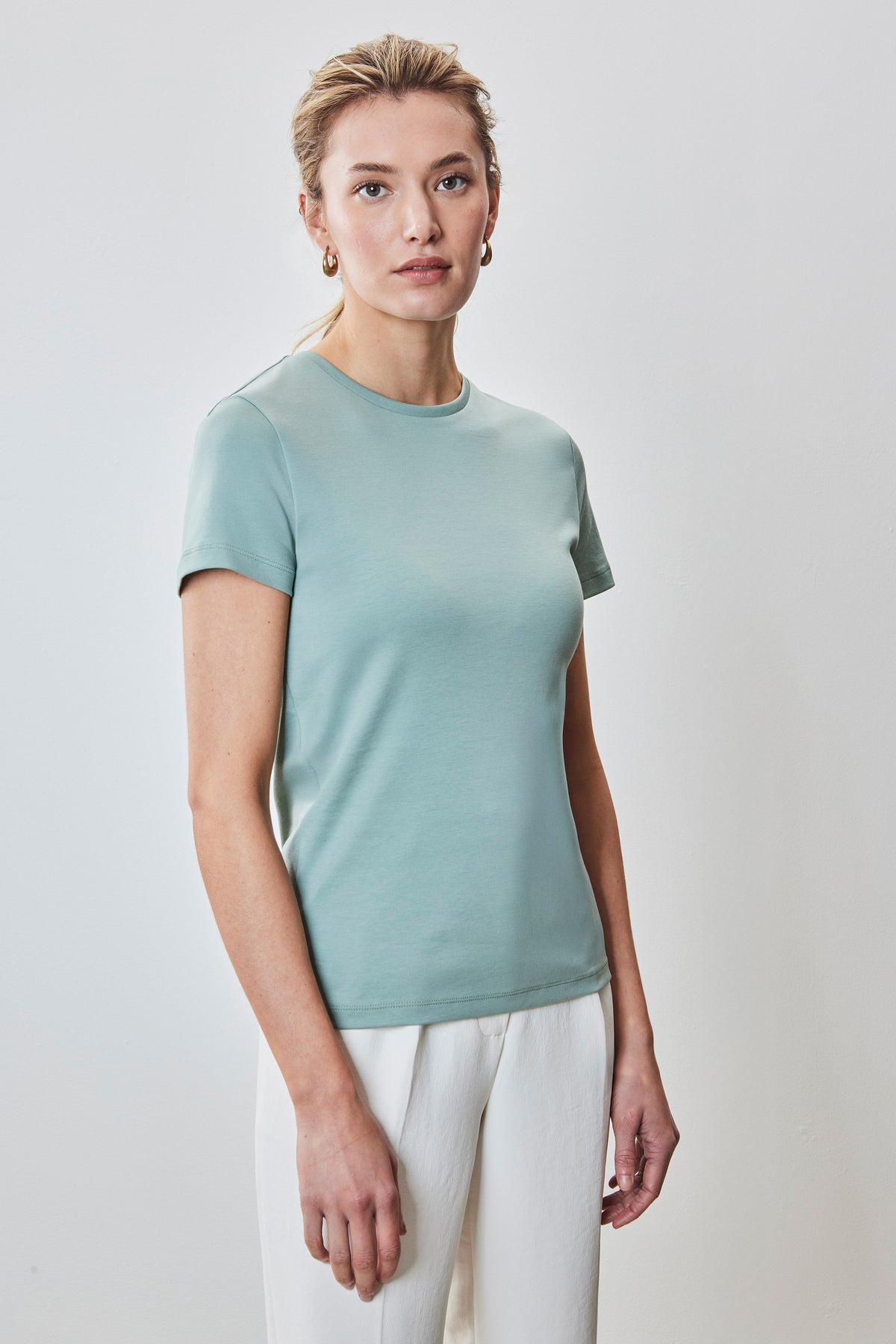 Woman wearing a sage green crew neck t-shirt with short sleeves and white pants.