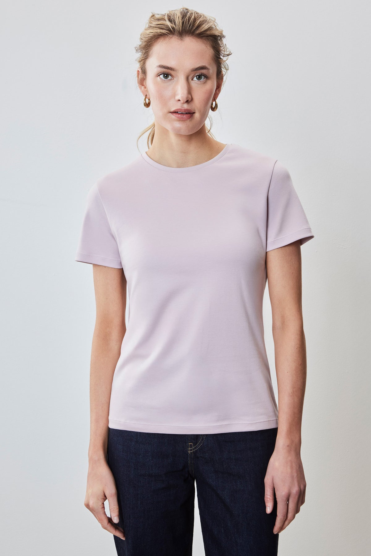 Woman wearing a light pink crew neck short-sleeve t-shirt with dark denim jeans.