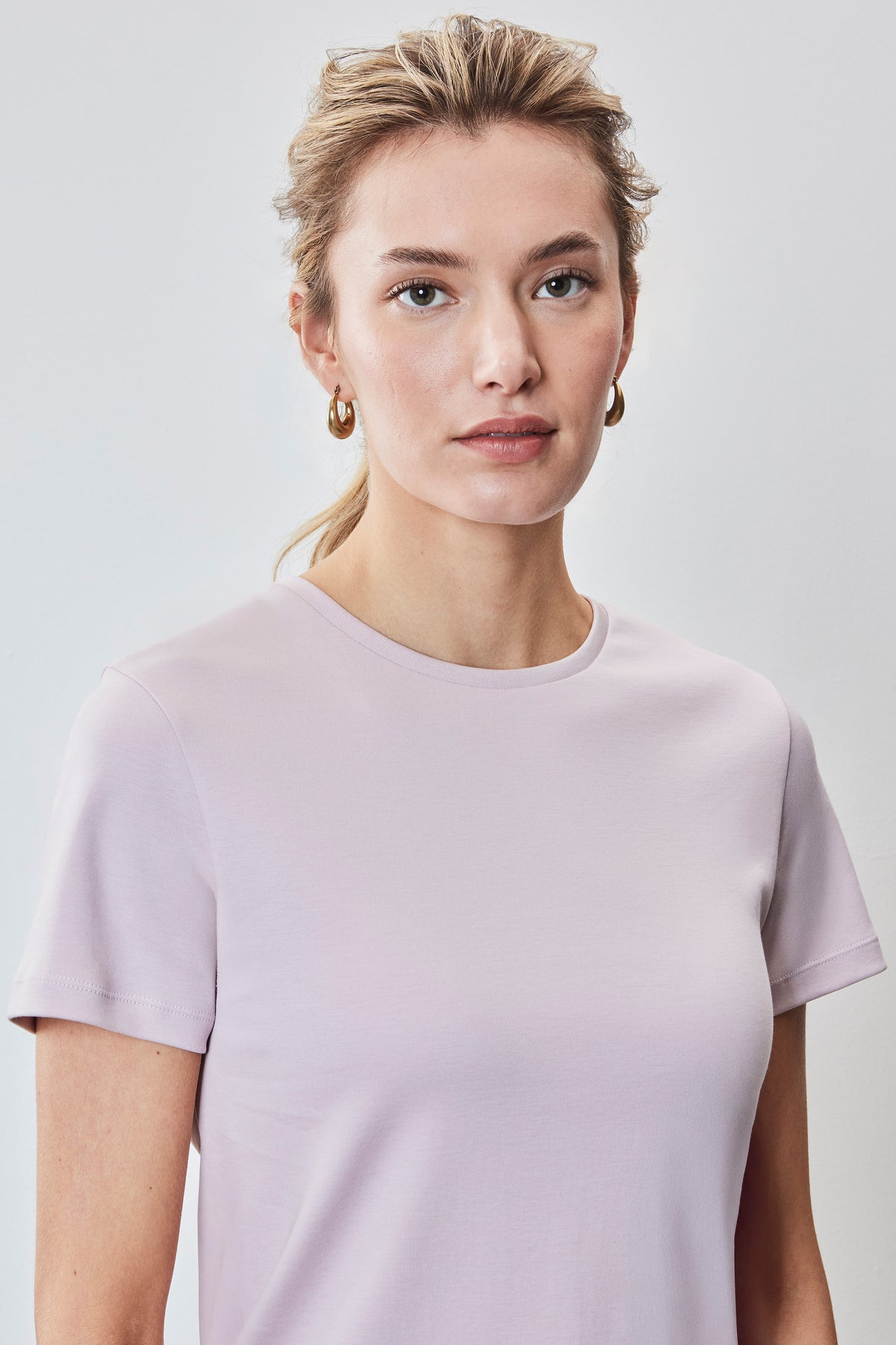 Woman wearing a light pink crew neck t-shirt with short sleeves against a neutral background.
