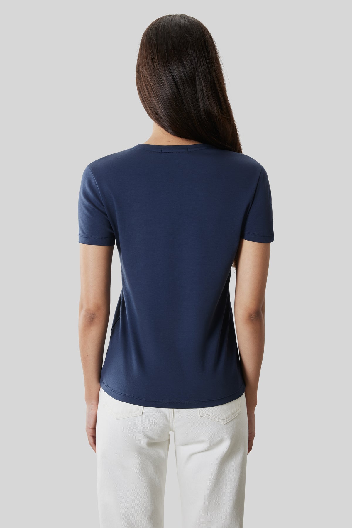 Woman wearing a navy blue short-sleeve crew neck tee paired with white pants, shown from the back.