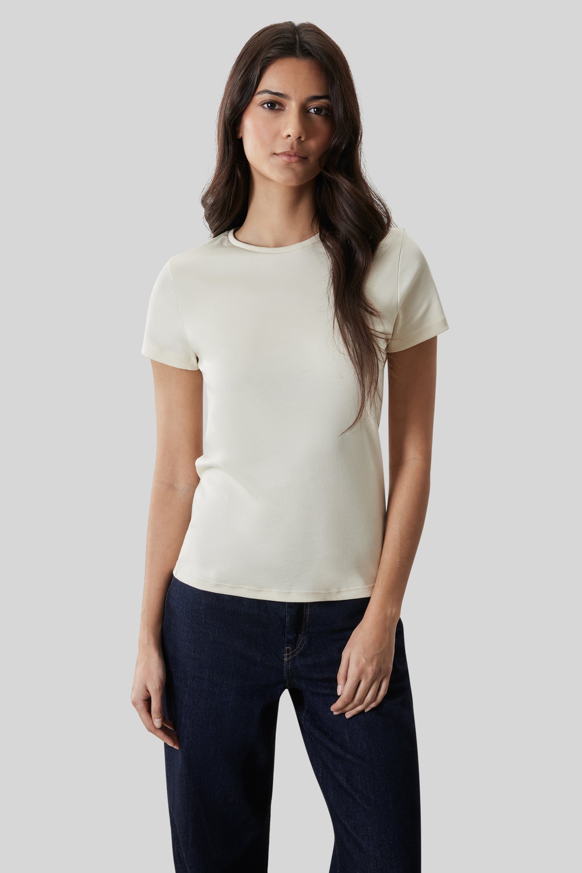 Woman wearing a cream-colored short-sleeve crewneck tee with dark blue jeans.