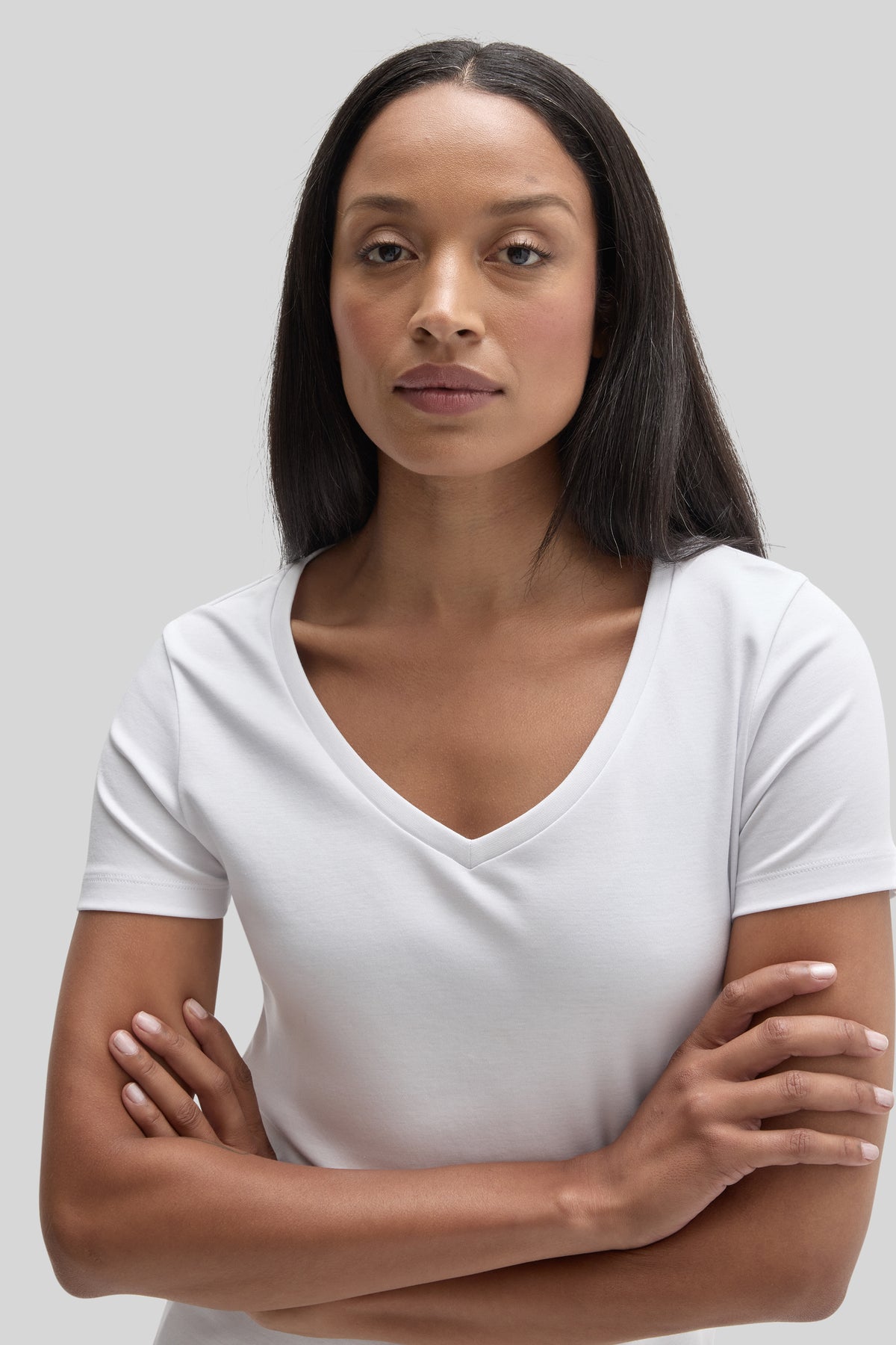 Woman wearing a white short-sleeve V-neck tee with arms crossed against a neutral background.